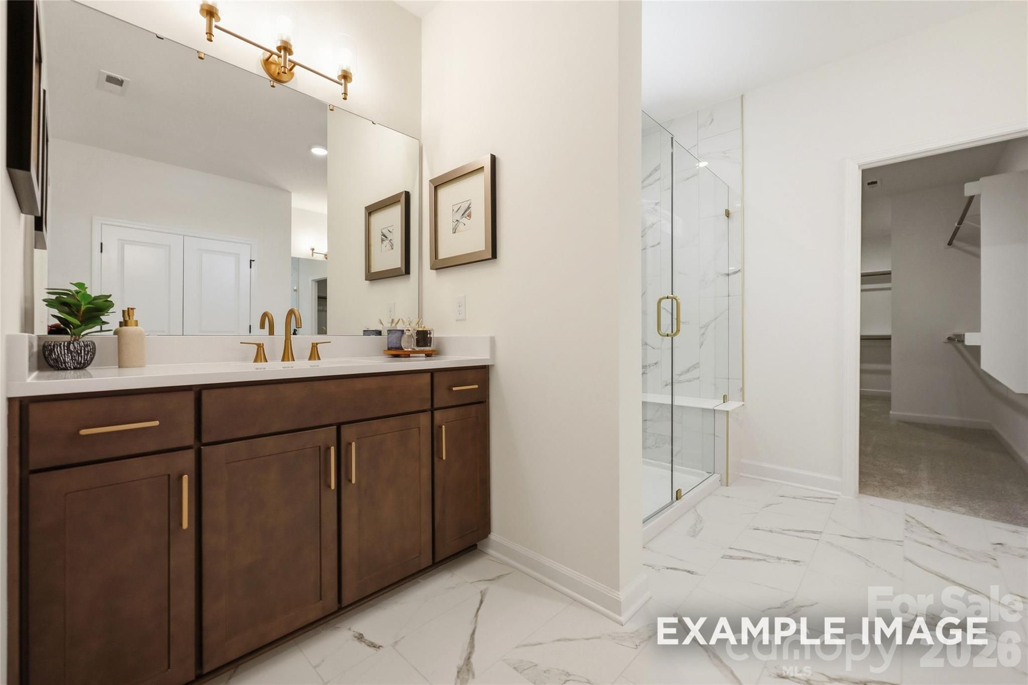 Elegant primary bathroom with dark wood double vanity, gold fixtures, marble tile shower, and walk-in closet in Davidson Homes Aspen B, Mooresville NC