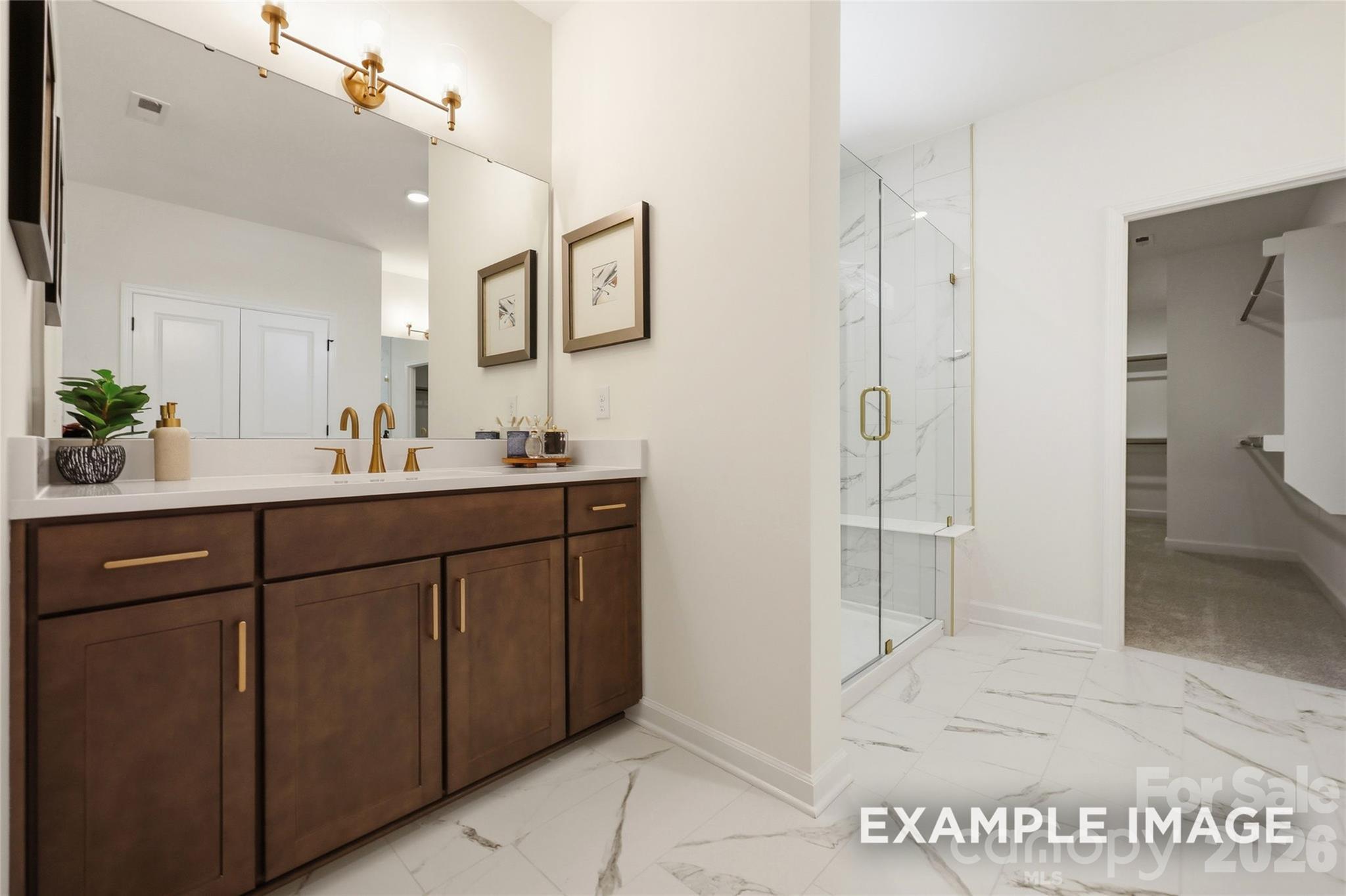 Elegant primary bathroom with dark wood double vanity, gold fixtures, marble tile shower, and walk-in closet in Davidson Homes Aspen B, Mooresville NC