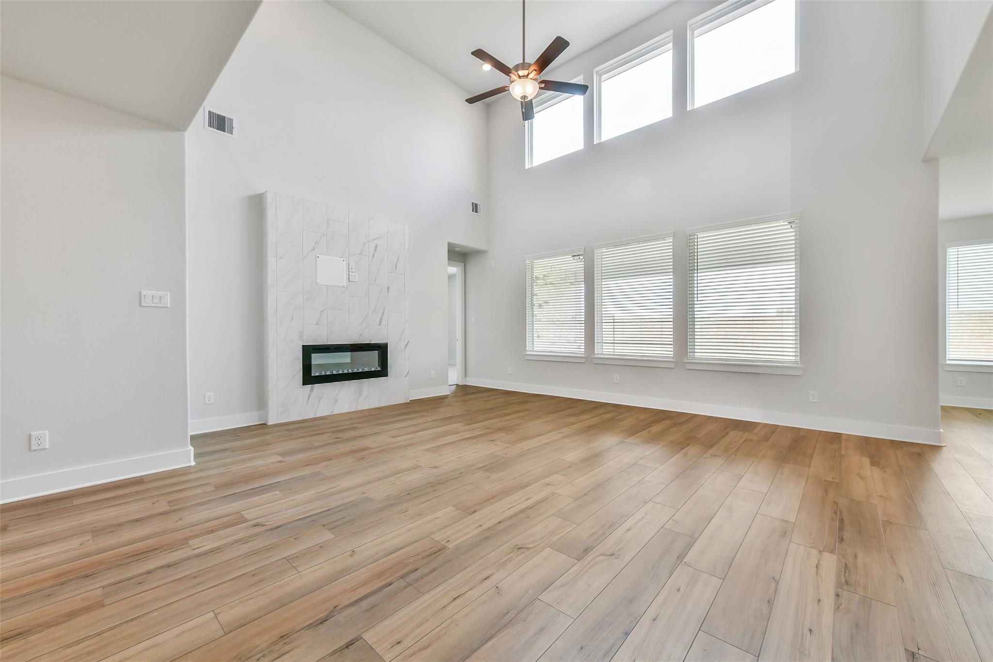 Spacious living room with vaulted ceiling, modern marble fireplace, large windows, hardwood floors in Davidson Homes The Victoria A, Lago Mar, Texas City