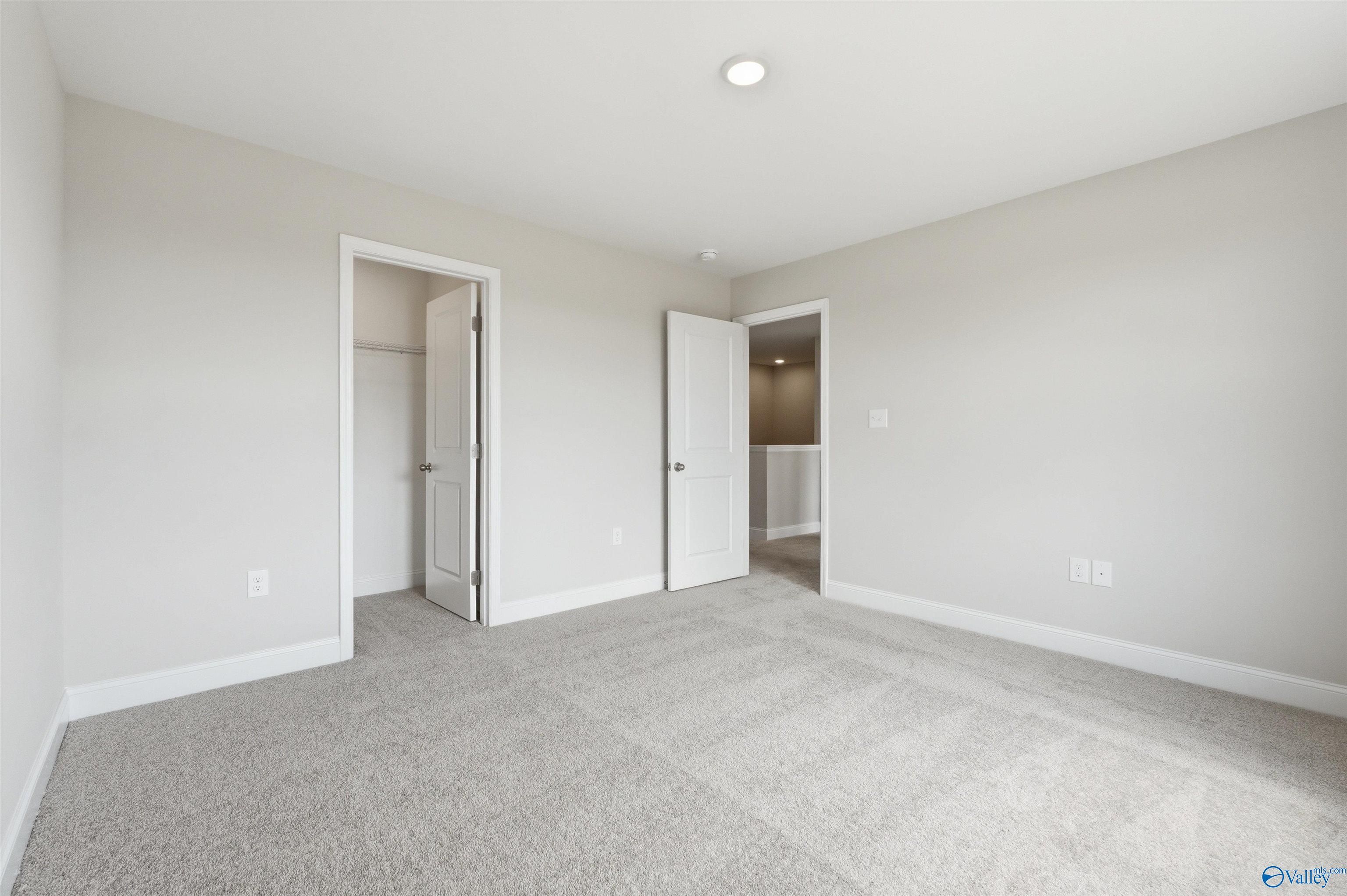 Bright bedroom with neutral carpet and walk-in closet in The Shelby D plan at Evergreen Mill, Madison, Alabama.