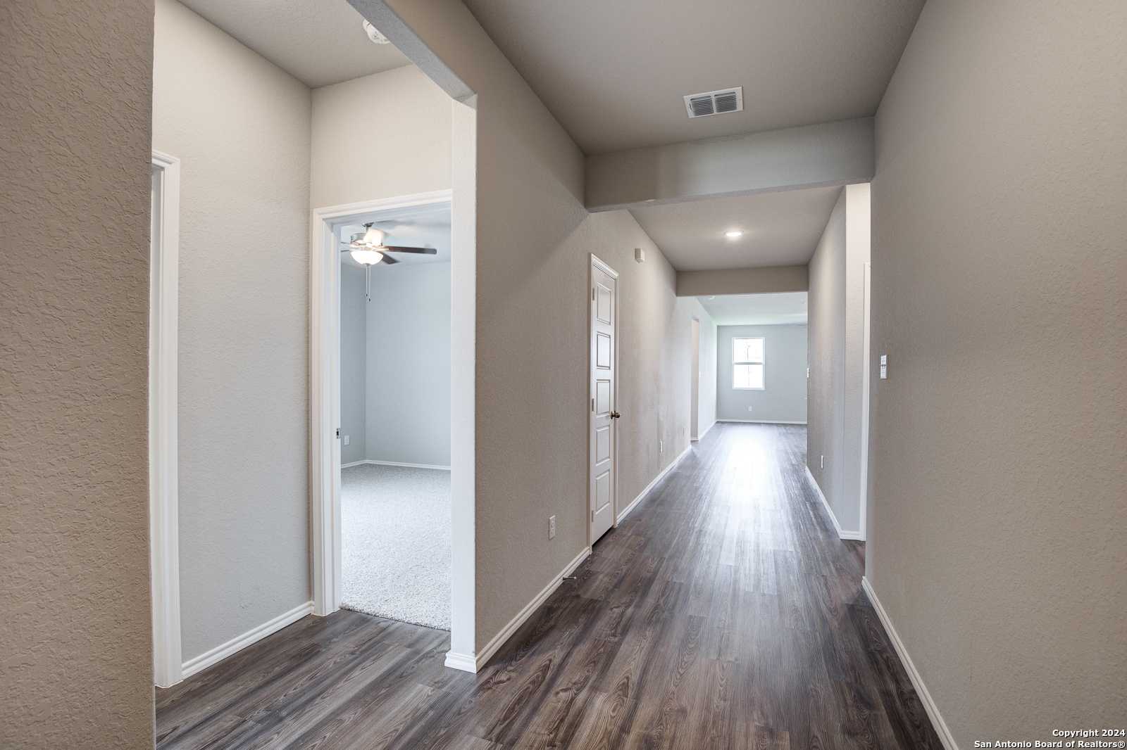 Spacious hallway with hardwood floors, neutral walls, and room doors in The Daphne J 4-bedroom home, Seguin, Texas