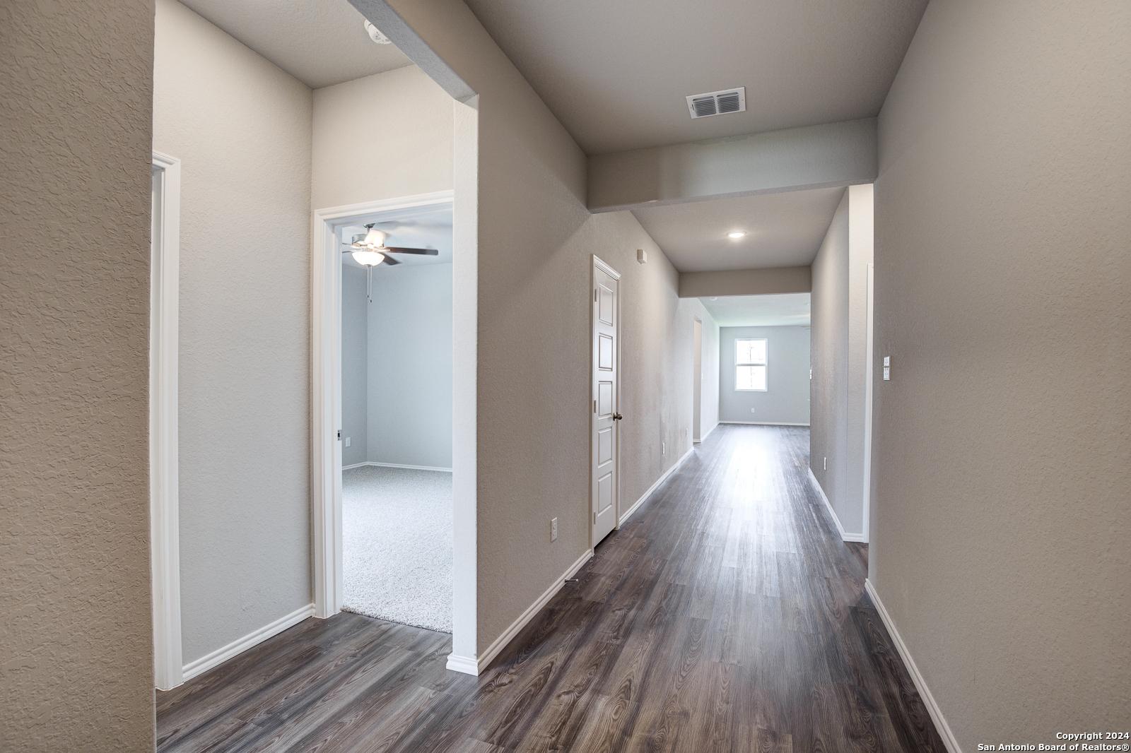 Spacious hallway with hardwood floors, neutral walls, and room doors in The Daphne J 4-bedroom home, Seguin, Texas