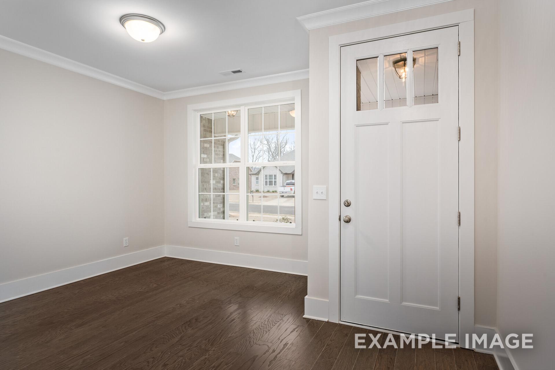 Spacious master bedroom in The Rockford with neutral walls, hardwood floors, large window, and white glass-paneled door