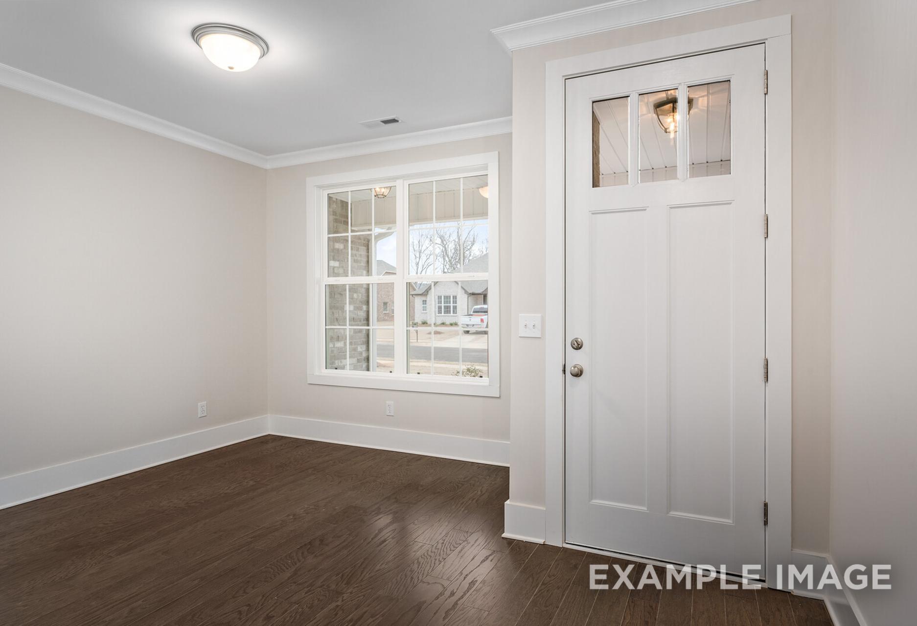 Spacious Rockford home interior with neutral walls, hardwood floors, large window overlooking trees, and white glass-paneled door