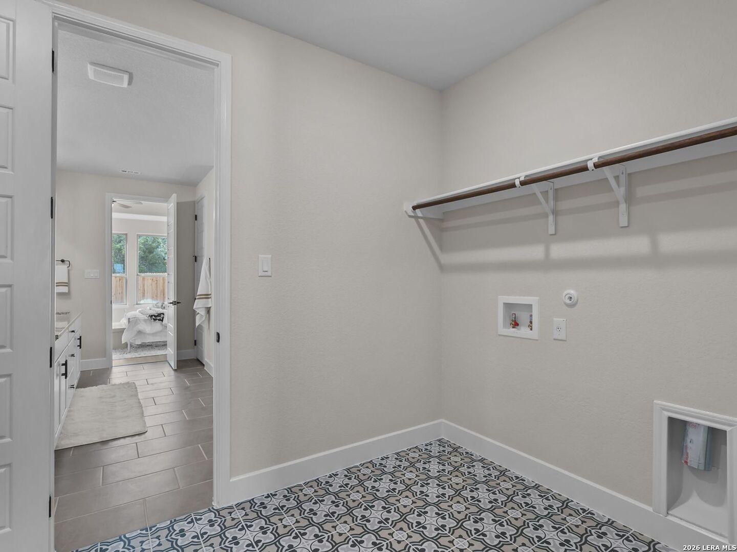 Laundry room with patterned tile flooring, shelving, and utility hookups in The Belmont H floor plan, Potranco Oaks.