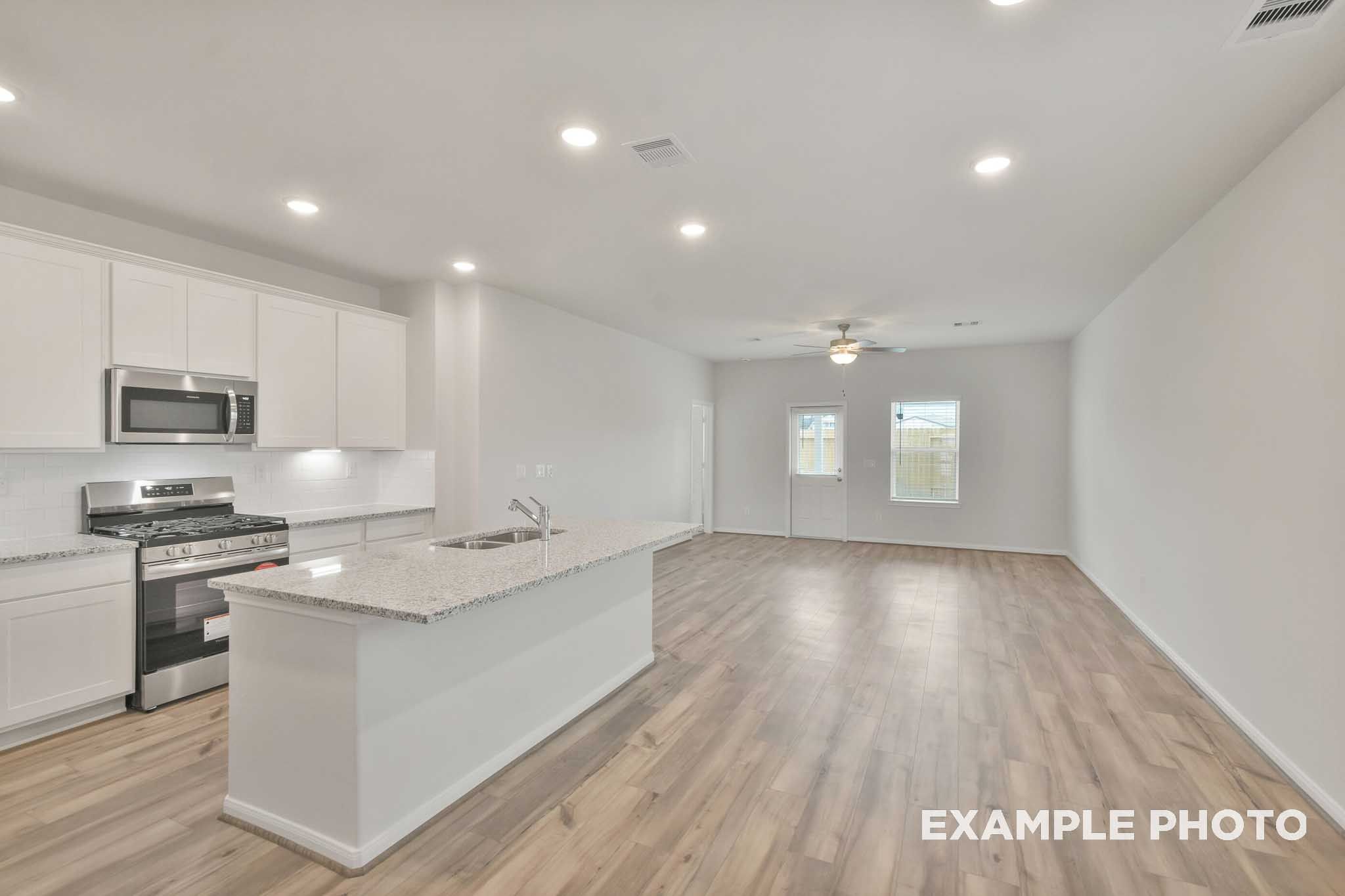 Open-concept kitchen and living area in The Brazos by Davidson Homes, featuring white cabinetry, granite island, and wood-look flooring