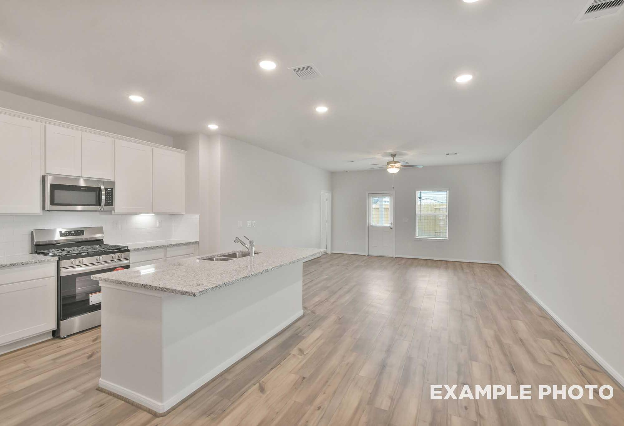 Open-concept kitchen and living area in The Brazos by Davidson Homes, featuring white cabinetry, granite island, and wood-look flooring