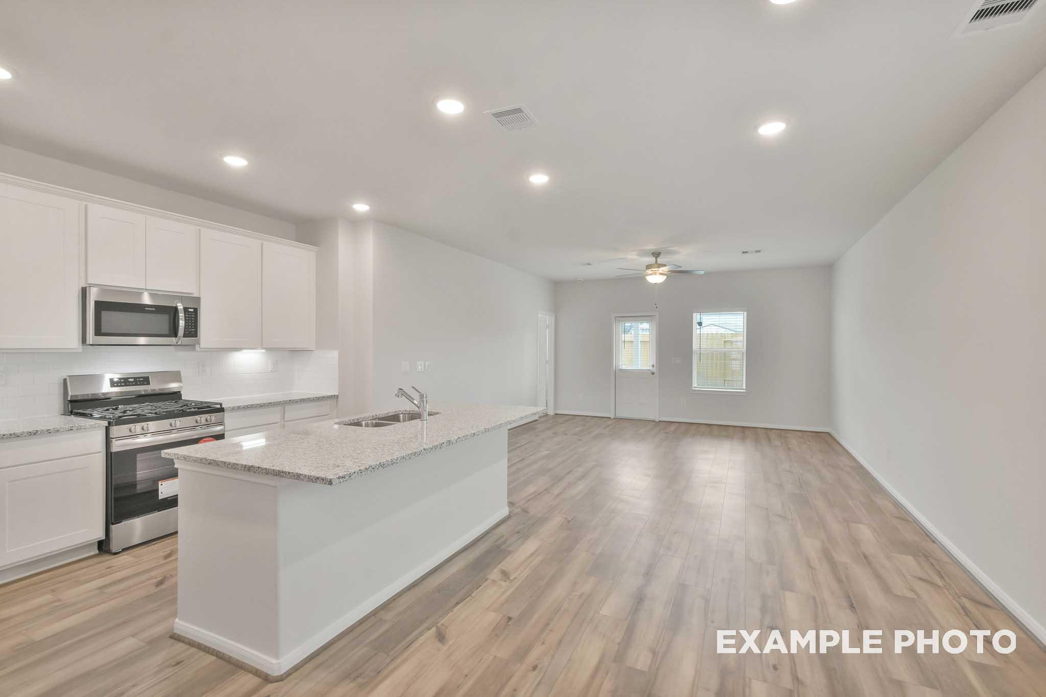 Open-concept kitchen and living area in The Brazos by Davidson Homes, featuring white cabinetry, granite island, and wood-look flooring