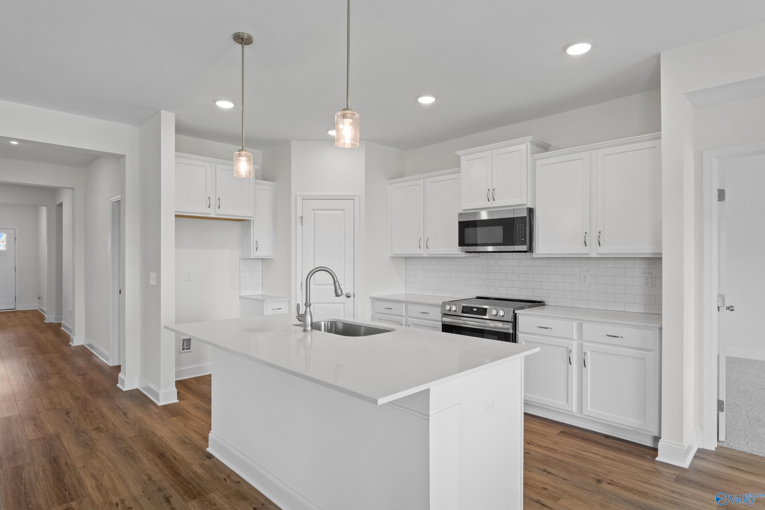 Modern white kitchen with island, quartz countertops, and stainless appliances in The Everett B floor plan, Athens, Alabama.
