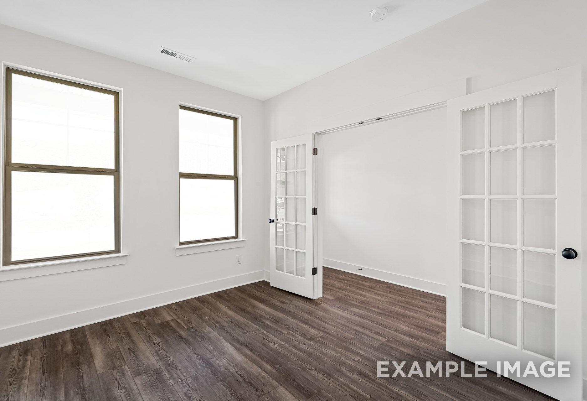 Spacious master suite in The Logan A featuring hardwood floors, large windows, and open French doors