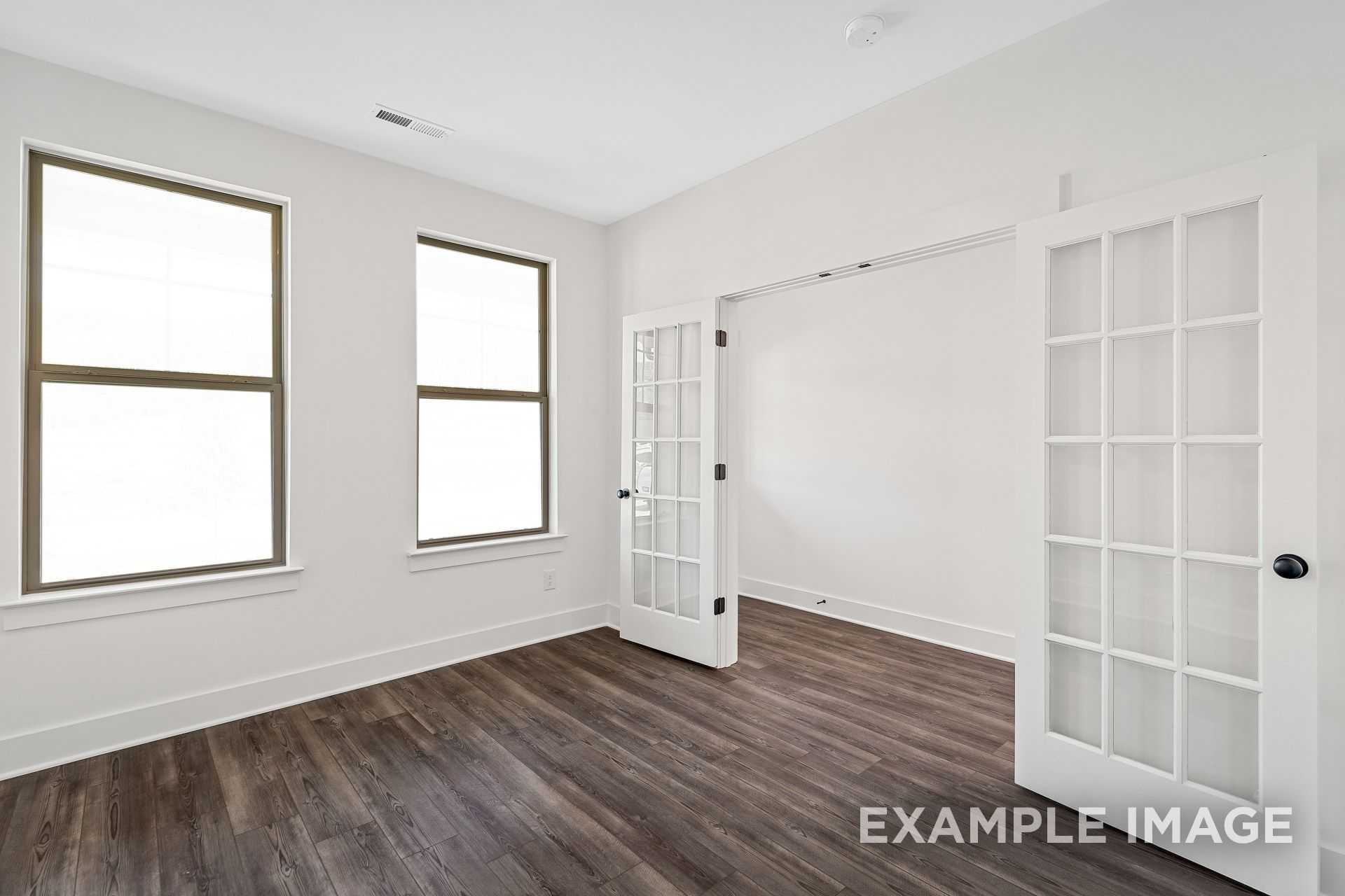 Spacious master bedroom in The Logan B home design with large windows, open double doors, and hardwood floors