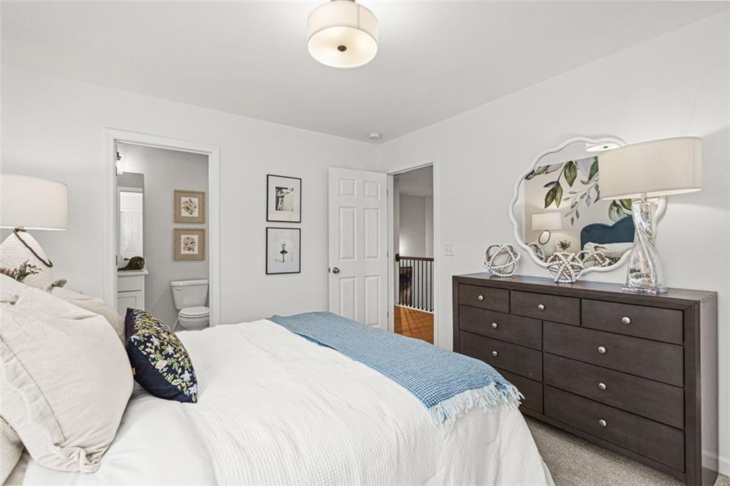 Cozy bedroom with plush white bed, blue throw, wooden dresser, and open bathroom door in Davidson Homes The Hickory B, Hoschton, GA