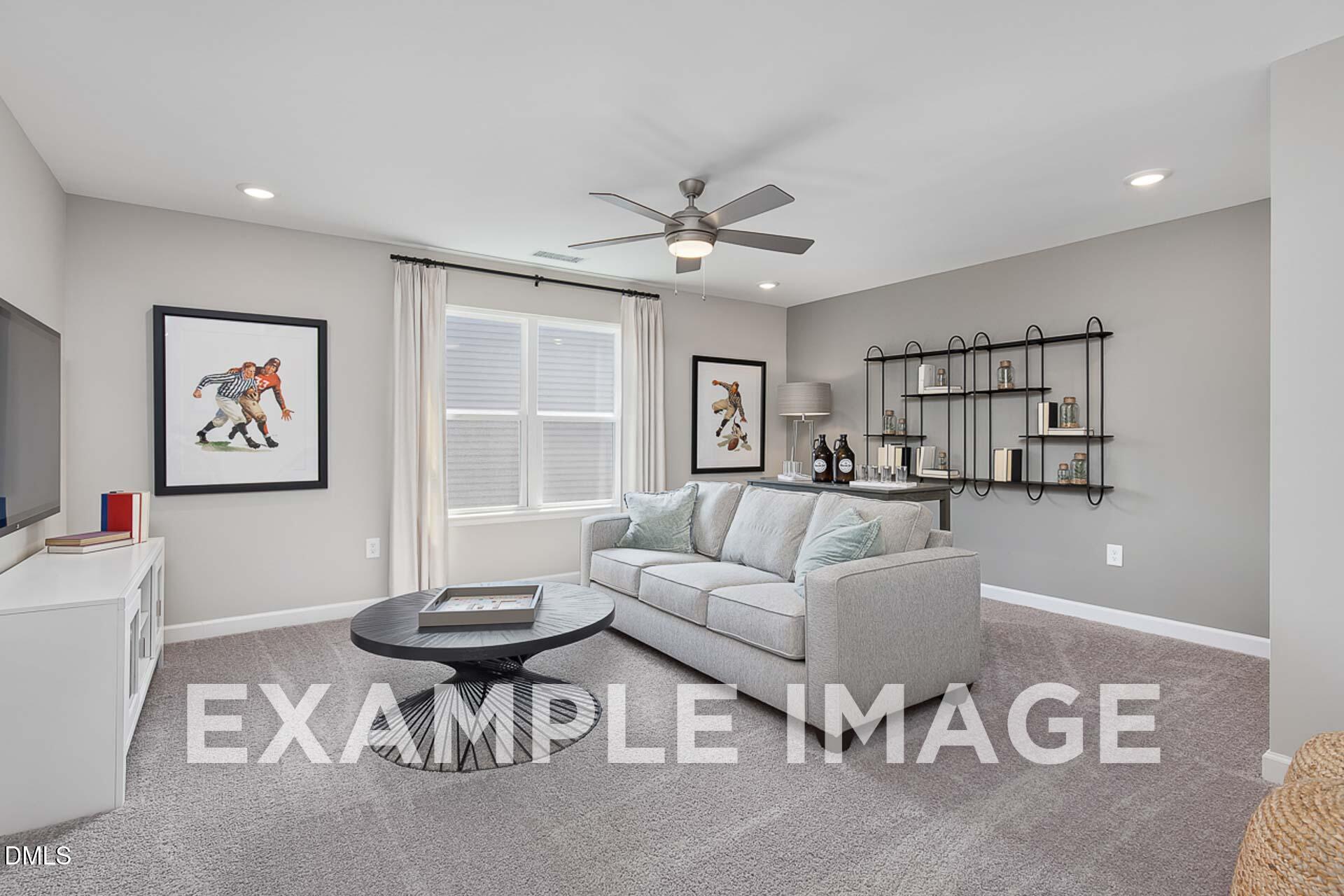 Cozy living room with gray sectional sofa, ceiling fan, large windows, and built-in shelves in Davidson Homes The Ash B, Lillington, NC