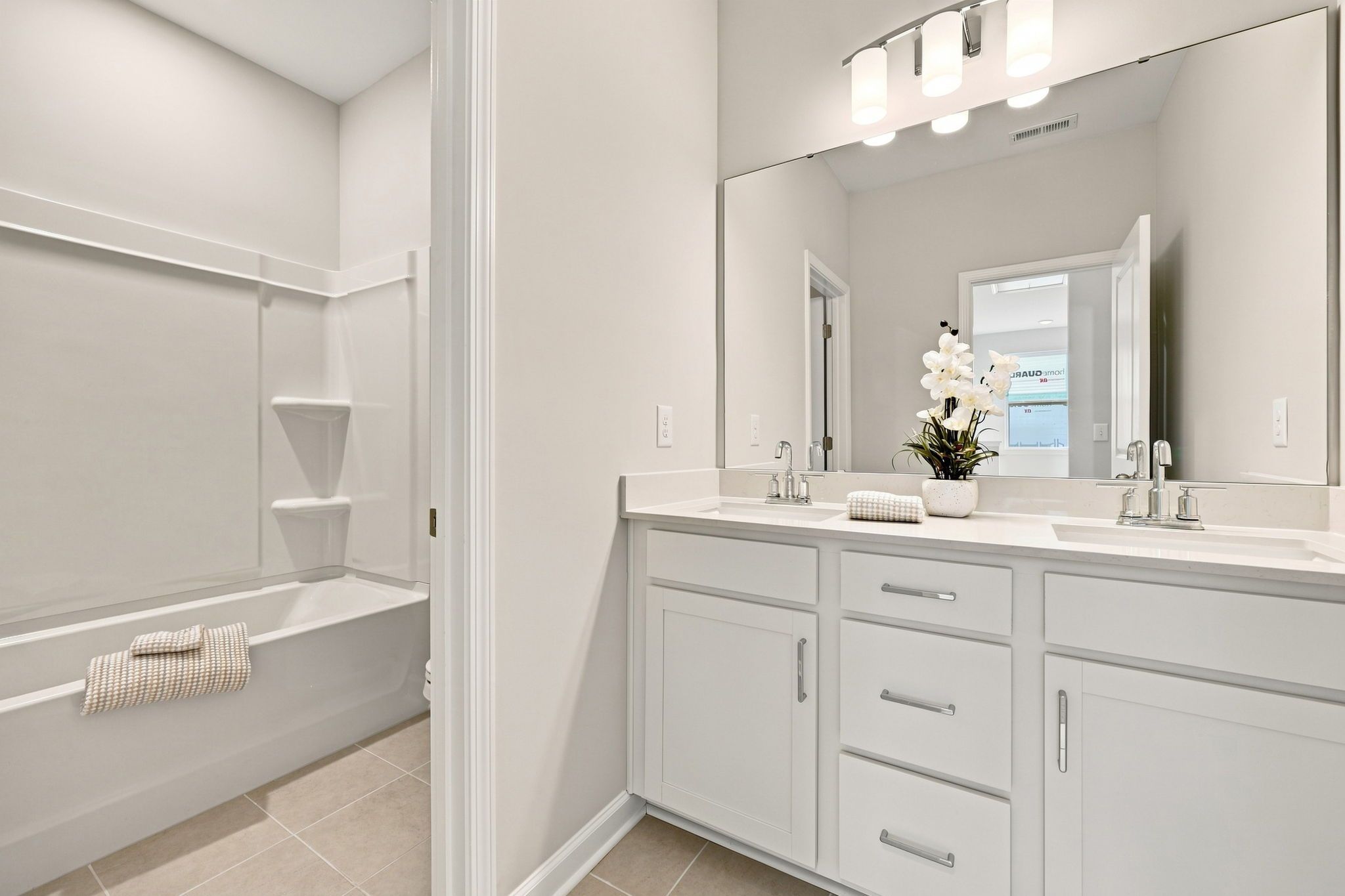 Modern bathroom in The Jordan featuring a dual-sink white vanity, large mirror, and tub-shower combo.