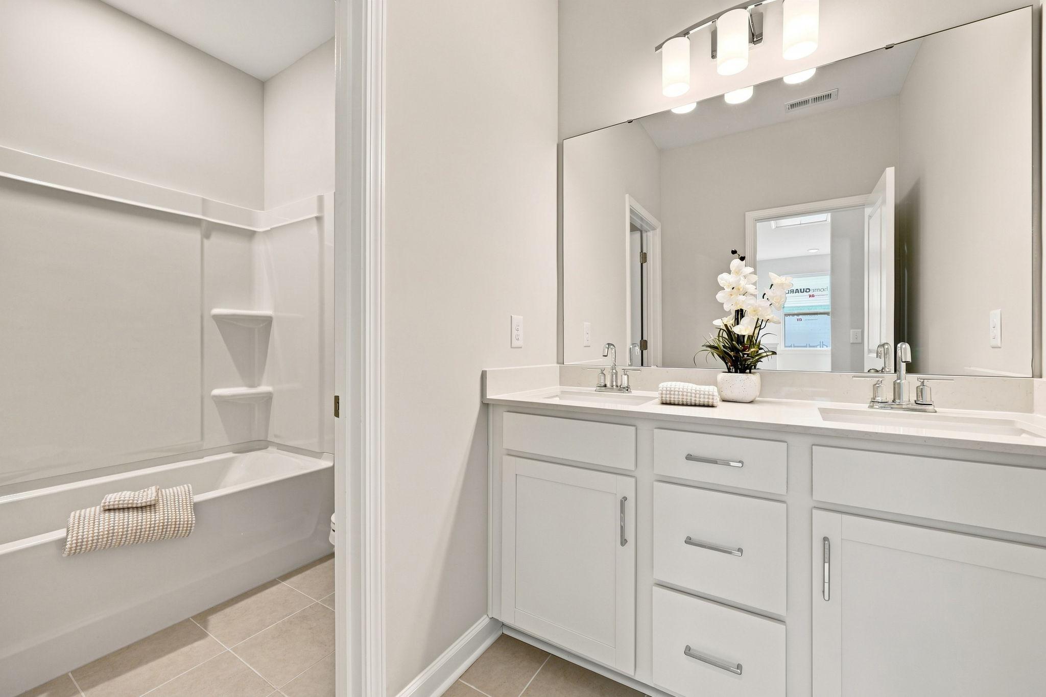 Modern bathroom in The Jordan featuring a dual-sink white vanity, large mirror, and tub-shower combo.