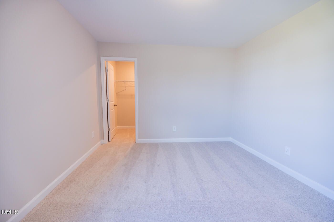 Empty bedroom with beige walls, plush carpet, and open door to adjoining bathroom in Davidson Homes The Hickory II C, Zebulon, NC