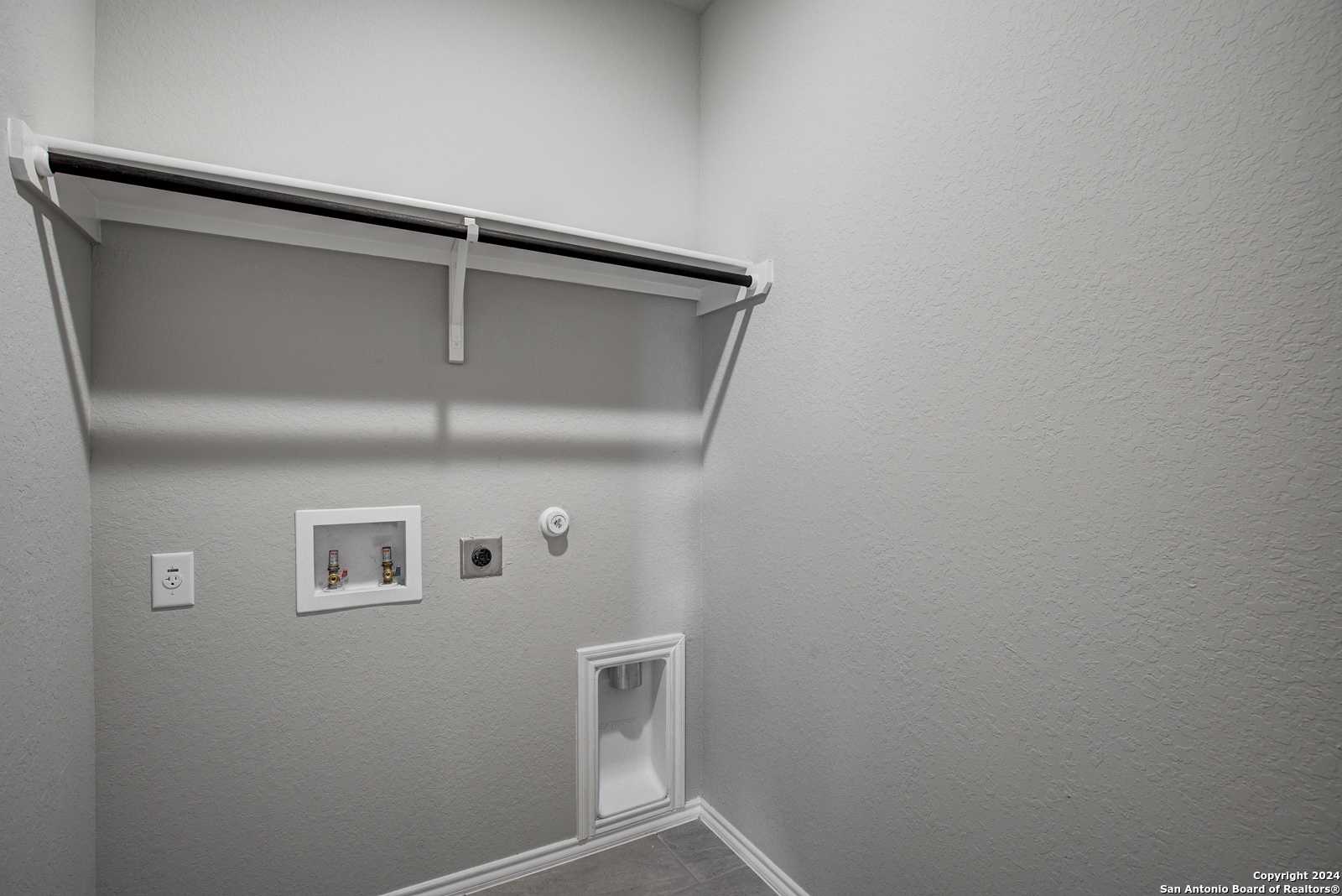 Modern laundry room with built-in white shelf, washer/dryer hookups in Davidson Homes The Daphne J, Seguin Texas