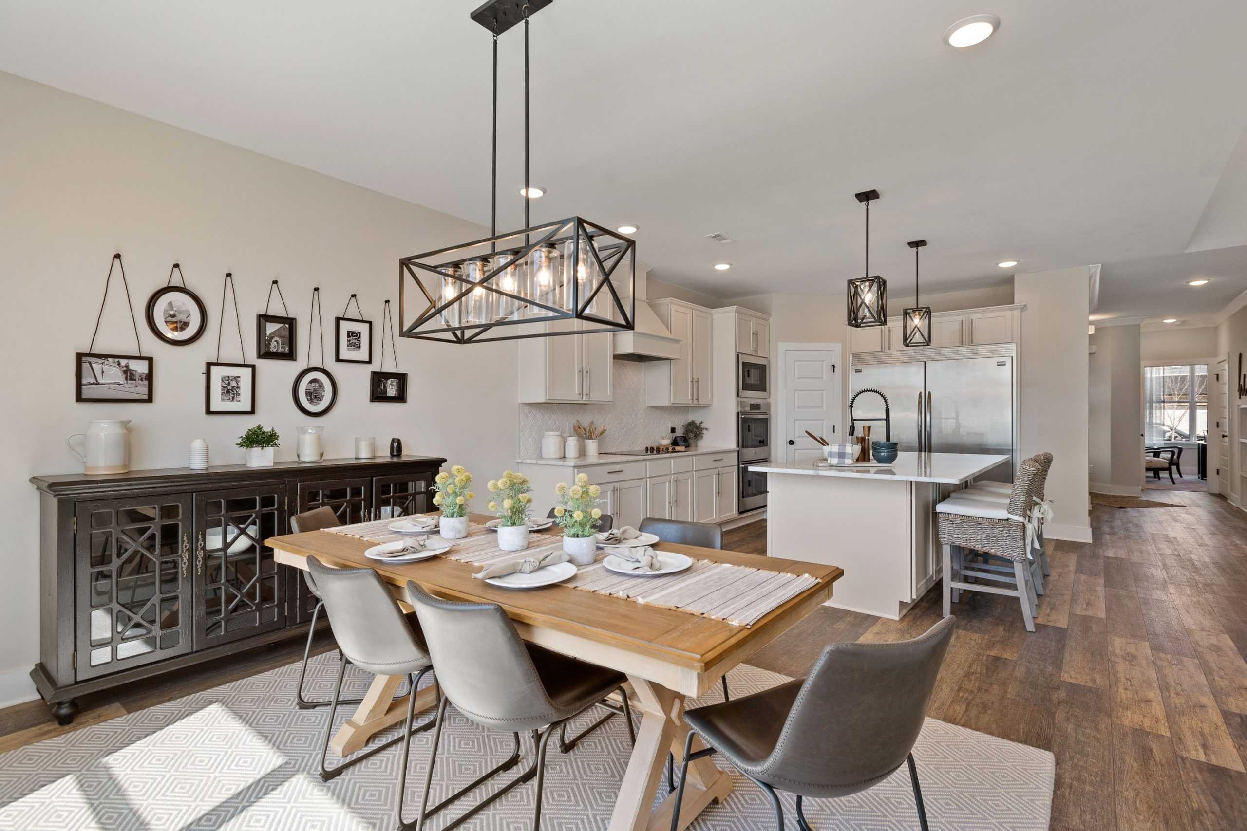 Open-concept kitchen dining area in Rivers Edge Murfreesboro TN home featuring farmhouse table, white cabinets, black pendant lights
