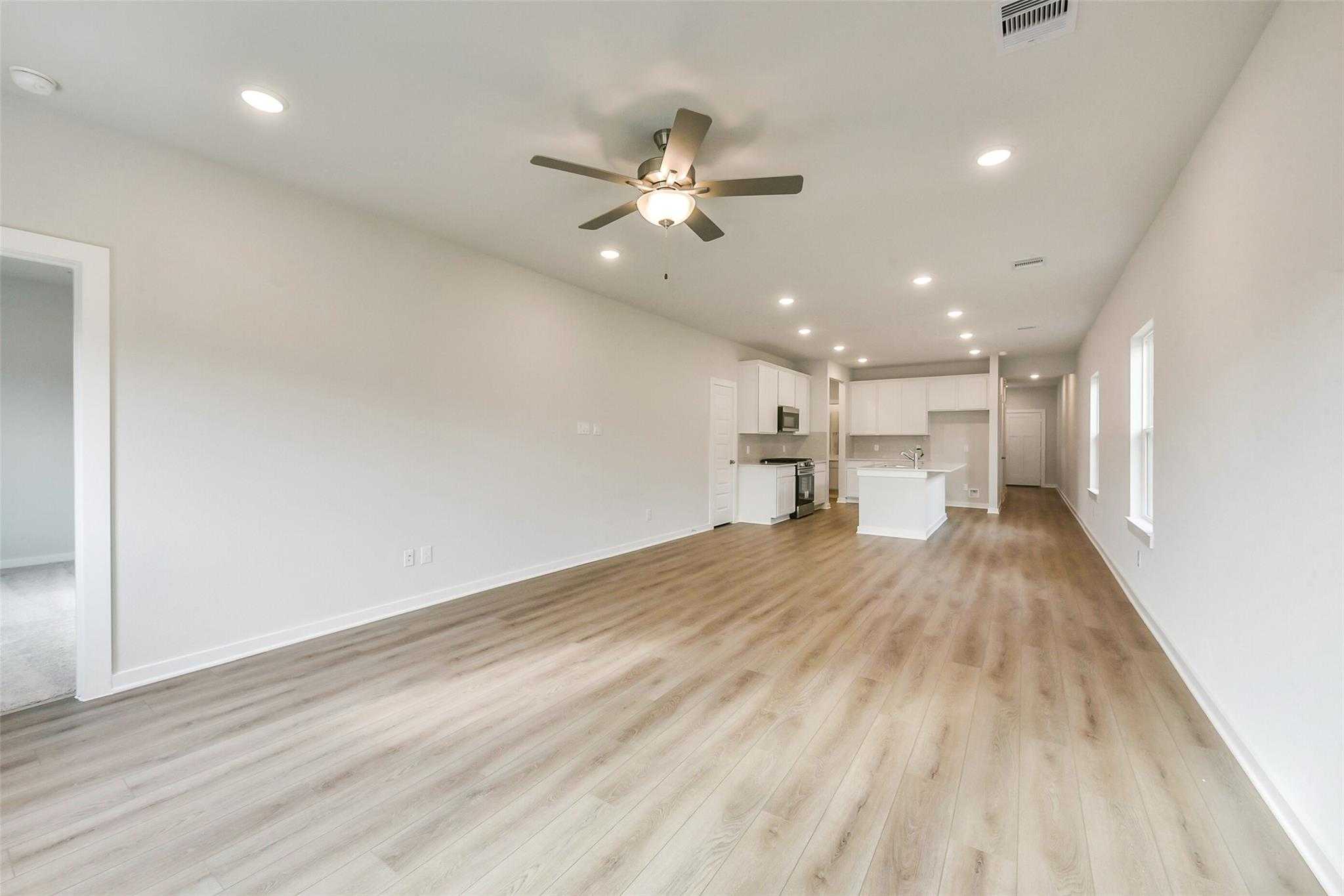 Open hallway with light wood flooring, ceiling fan, and recessed lights leading to white kitchen island in Davidson Homes The Frio G, Dayton Texas