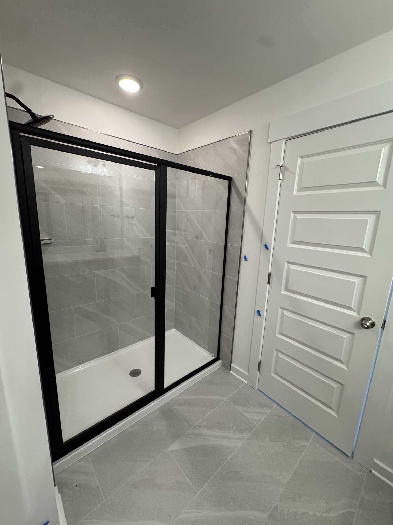 Modern glass shower with black frame, subway tile walls, and gray floor tile in Davidson Homes The Logan C master bath, Gallatin TN
