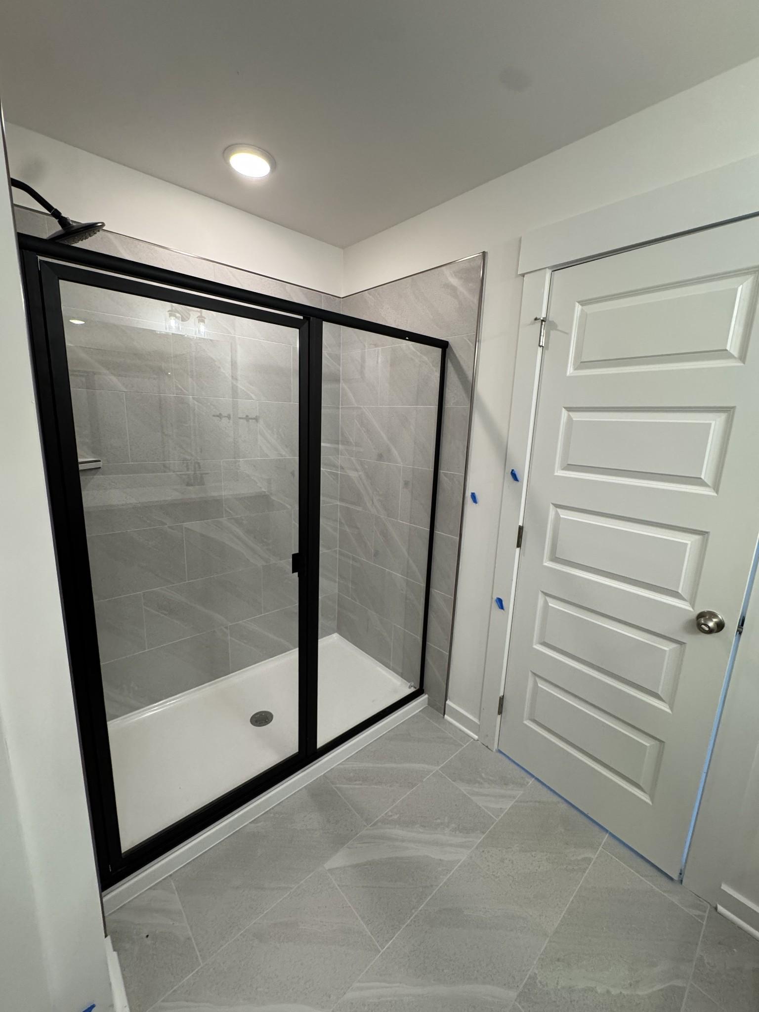Modern glass shower with black frame, subway tile walls, and gray floor tile in Davidson Homes The Logan C master bath, Gallatin TN