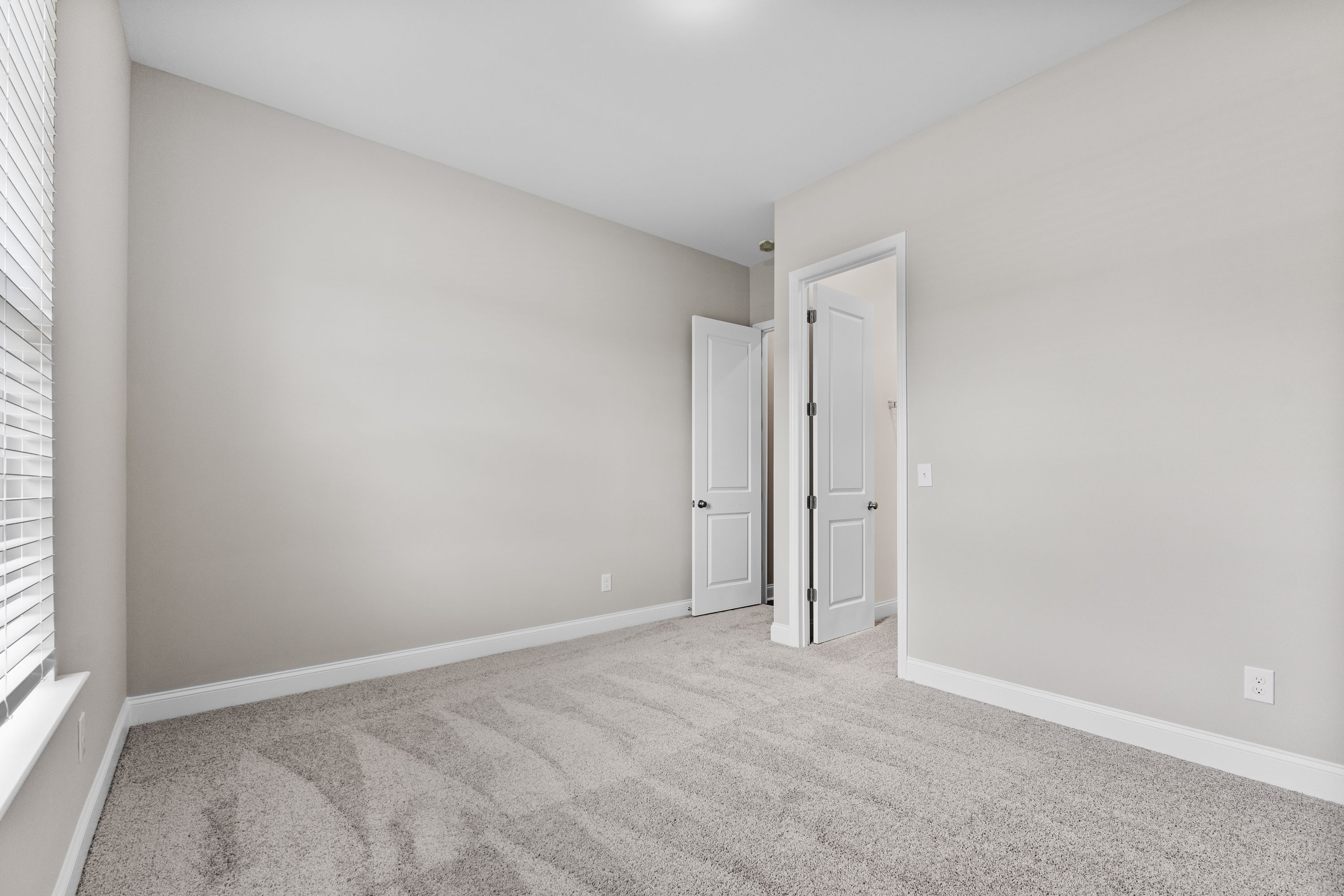 Spacious bedroom in The Arcadia E showcasing beige walls, neutral carpet flooring, and double doors to closet and bath