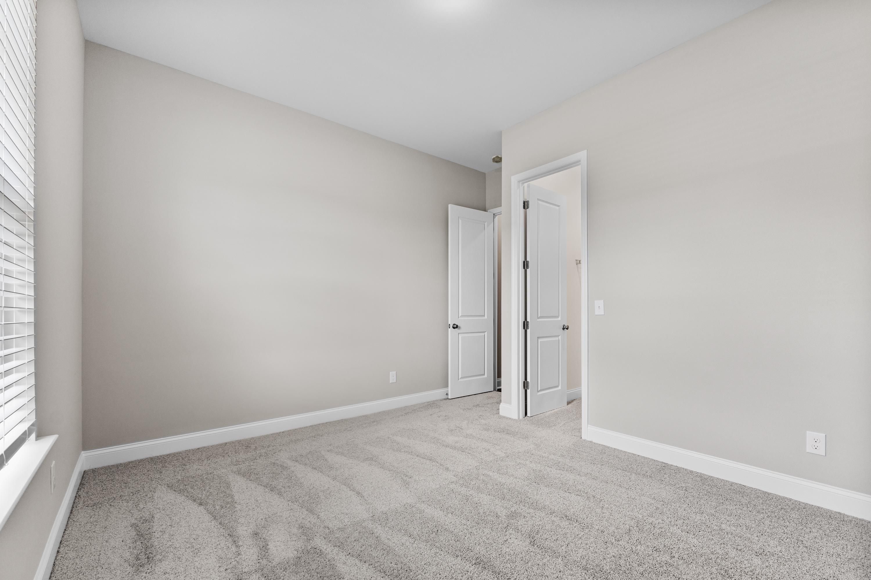 Spacious empty bedroom in The Arcadia B by Evermore Homes featuring beige walls, carpeted floor, double doors, and window blinds