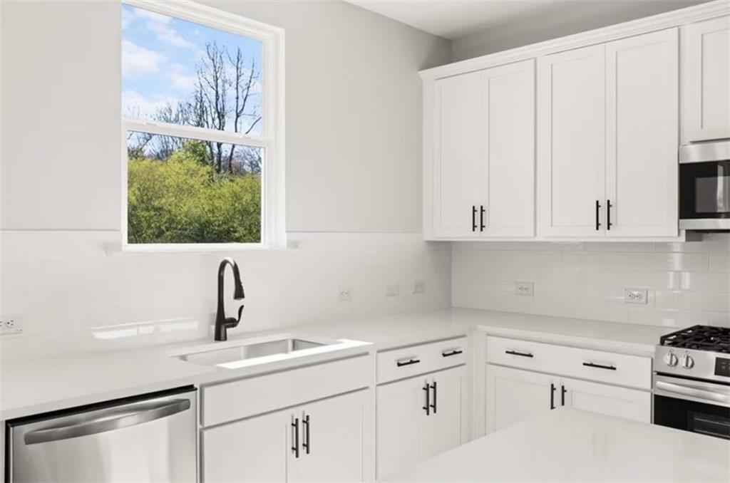 Bright kitchen with white shaker cabinets, quartz counters, stainless appliances, and garden-view window in The Hickory B, Winder GA