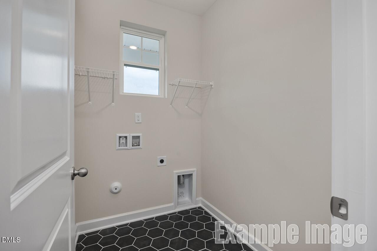 Modern laundry room with utility sink, hanging rods, window, and black hexagonal tile floor in Davidson Homes The Carter C, Lillington, NC