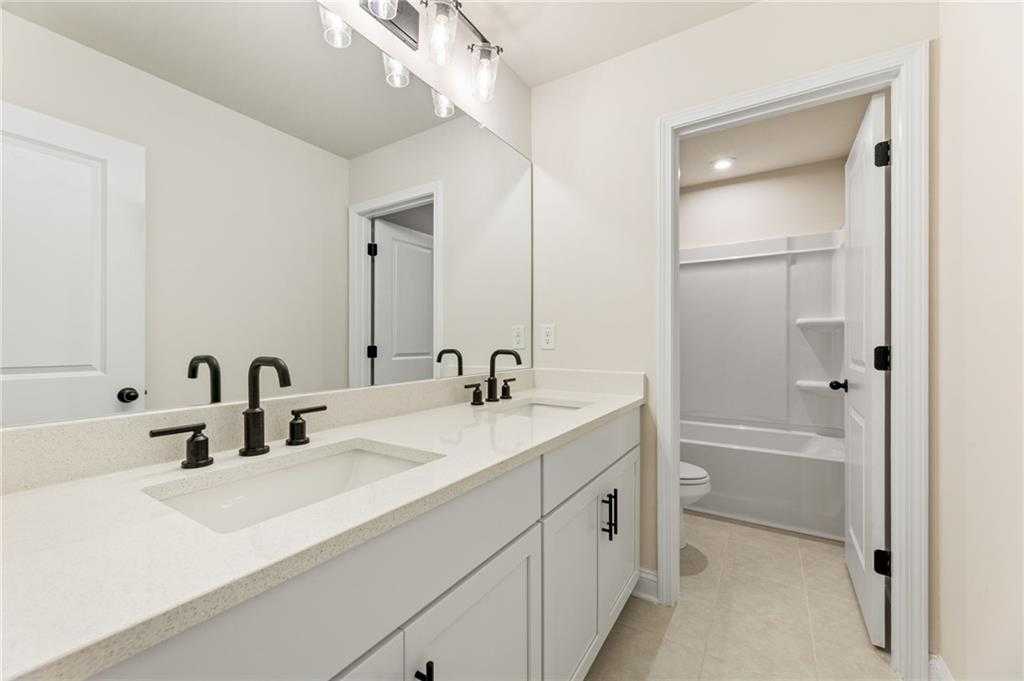Modern double vanity bathroom with white quartz counters, black faucets, and large mirror in The Hickory E by Davidson Homes, Buford, GA