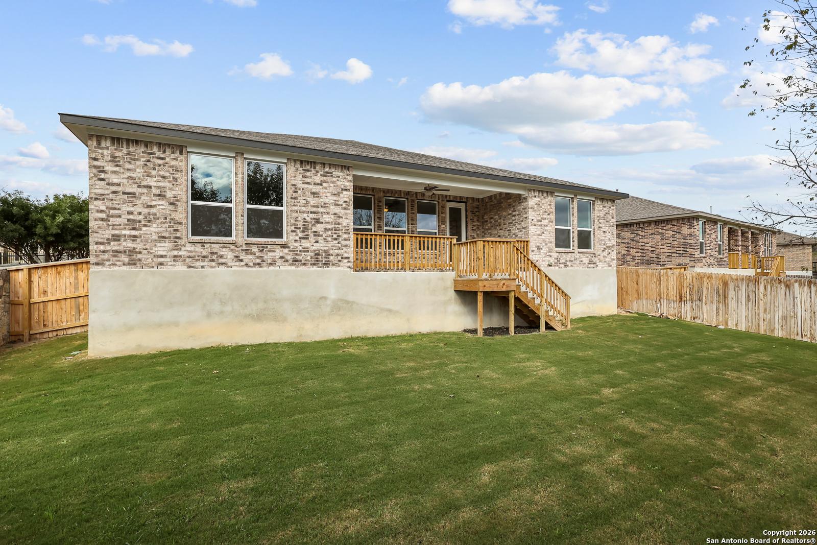 Backyard view of The Lanier H single-story brick home with covered porch, wooden deck stairs, and lush green lawn in Ladera, San Antonio by Davidson Homes