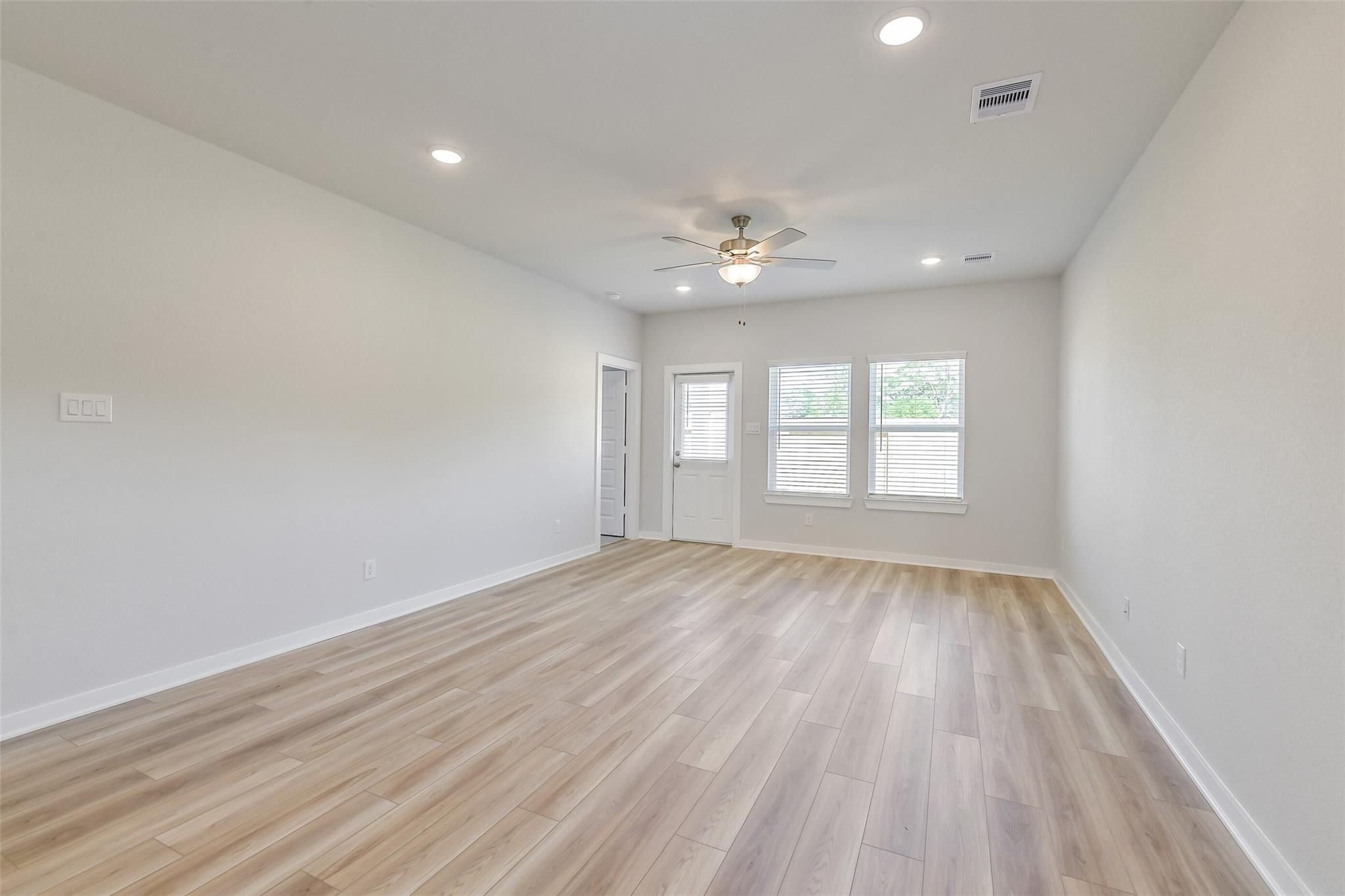Spacious living room with light oak laminate floors, ceiling fan, recessed lights, and large window views in Davidson Homes San Marcos E, Conroe Texas