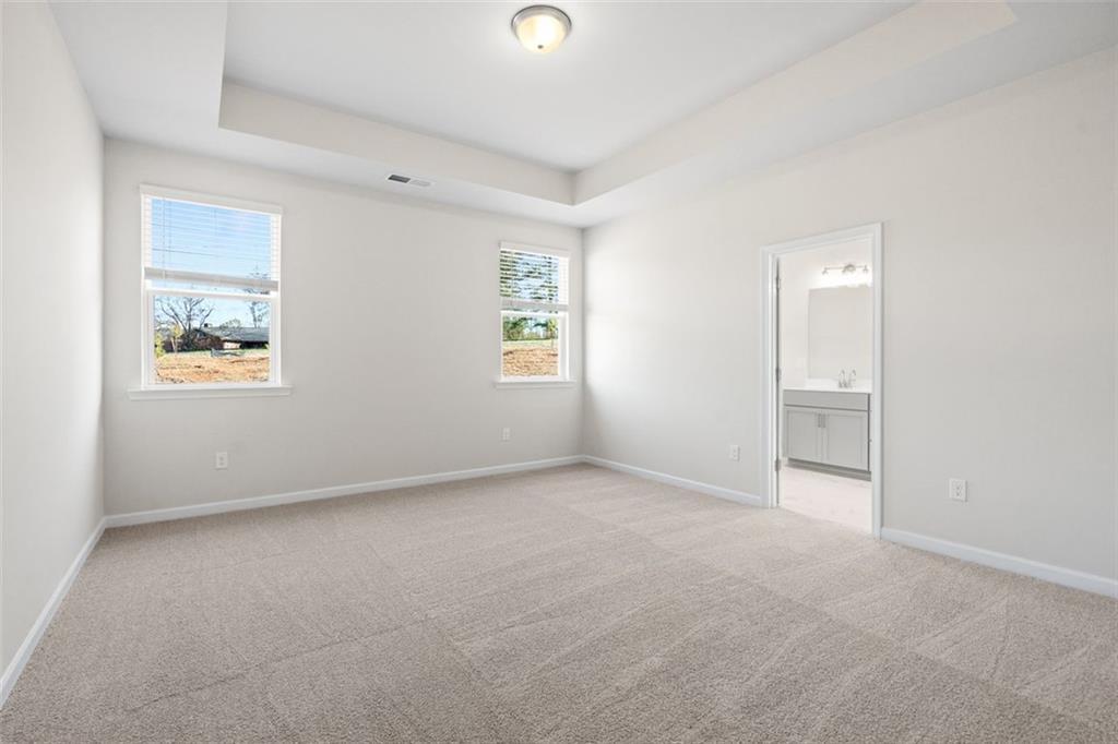 Bright secondary bedroom with large windows, beige carpet, and adjacent bathroom in Davidson Homes The Glenwood C at Wehunt Meadows, Hoschton