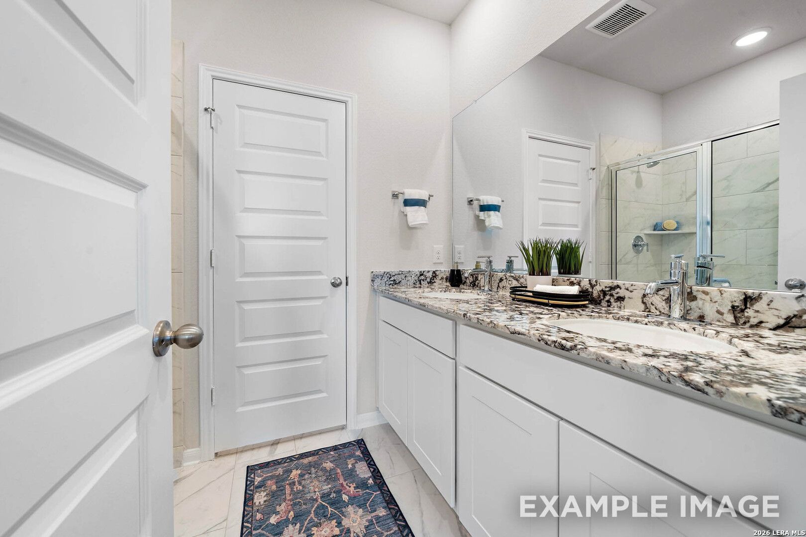 Modern bathroom with double vanity, granite countertops, and walk-in shower in The San Marcos F home in San Antonio, TX.