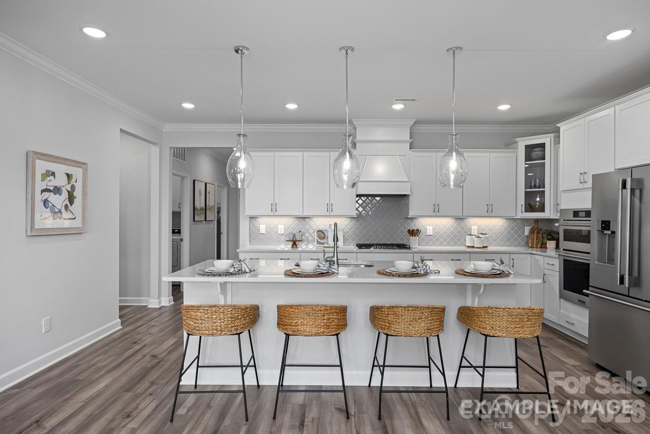Modern kitchen with white cabinets, quartz island, and rattan stools in The Magnolia A floor plan, Windgate, Mooresville.