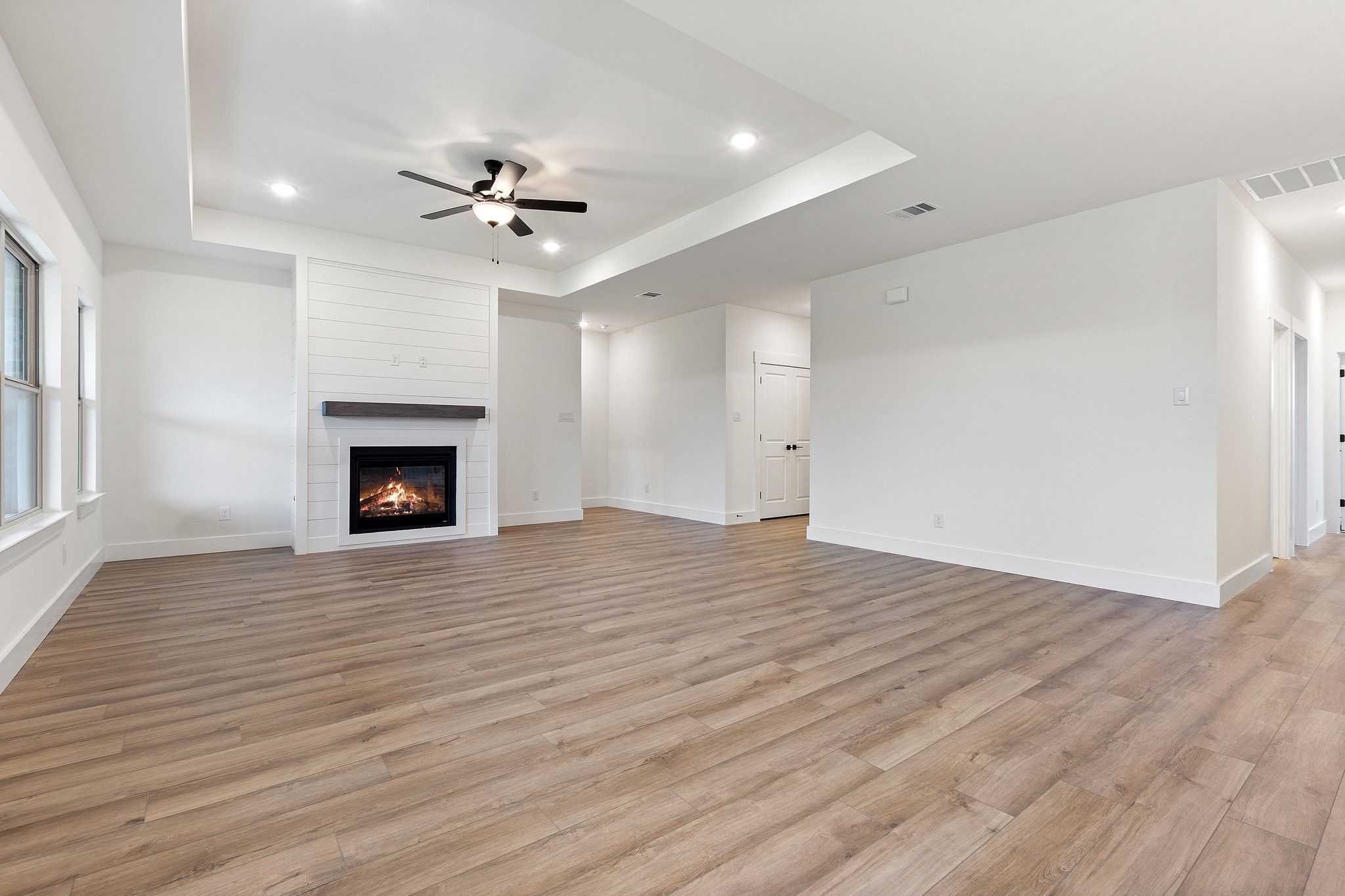Spacious living room with shiplap gas fireplace, hardwood floors, and ceiling fan in Davidson Homes The Rockford C, Josephine, Texas