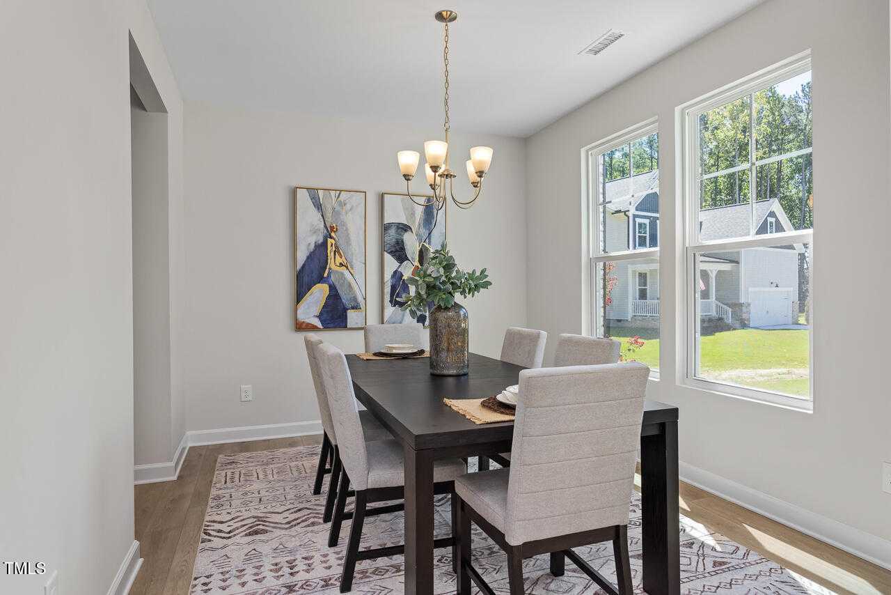 Elegant dining room with dark wood table, beige chairs, chandelier, abstract art, and backyard views in The Willow C home, Lillington, NC