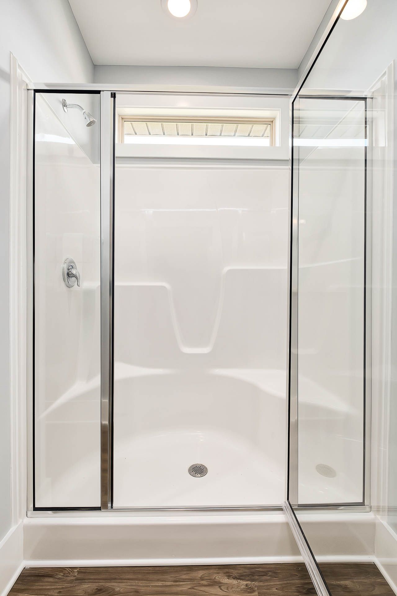 Modern walk-in shower with frameless glass doors in Heritage Heights bathroom, Madison AL, hardwood floors and transom window