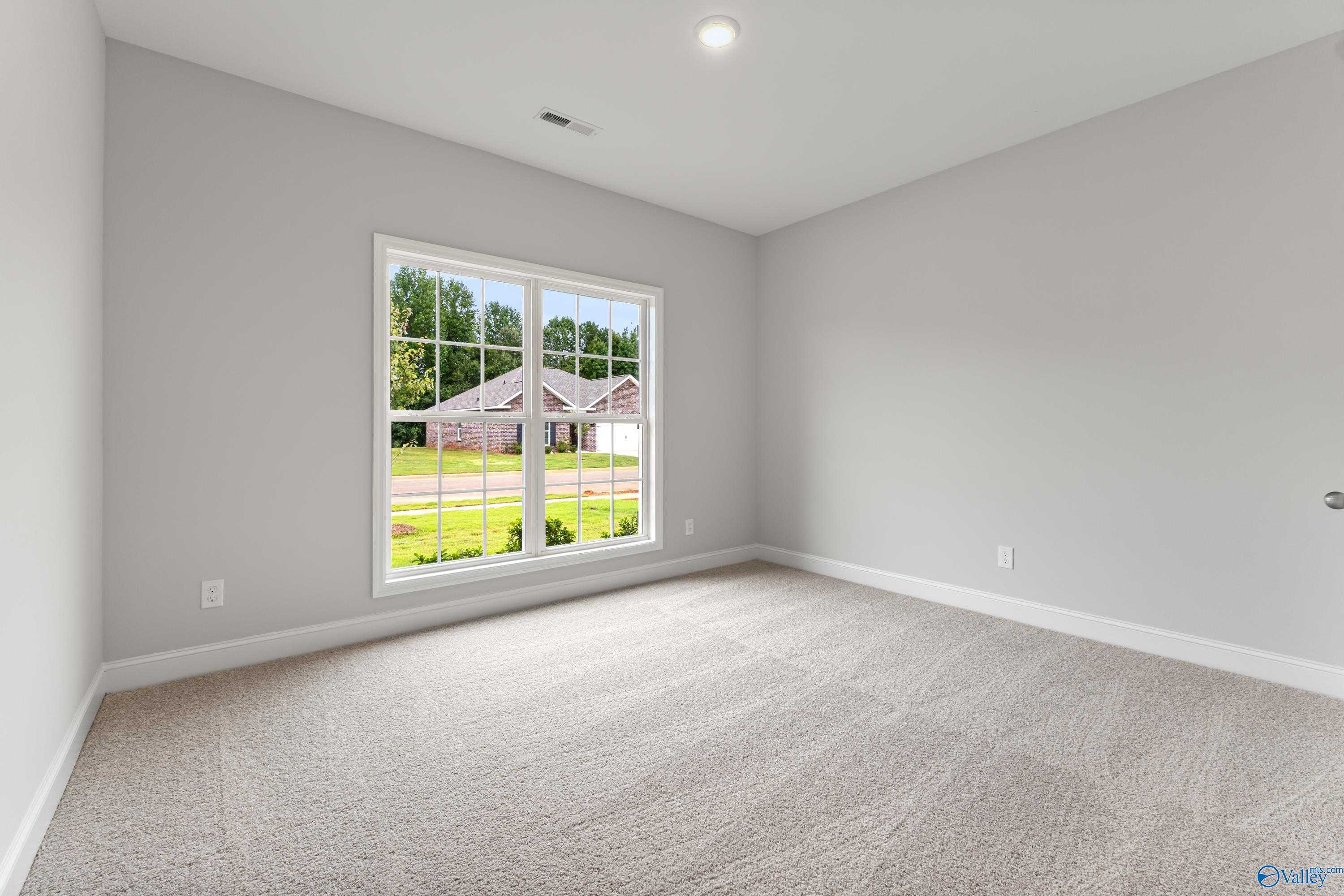 Bright bedroom with gray walls, beige carpet, and large window view of green lawn in Davidson Homes The Daphne C, Athens, Alabama