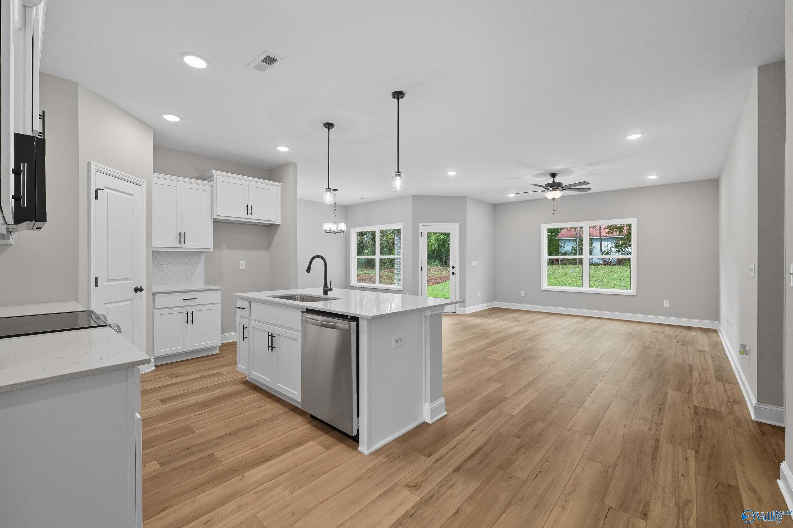 Open-concept kitchen featuring white island, hardwood floors, and large windows overlooking yard in Davidson Homes The Daphne, Meridianville, AL