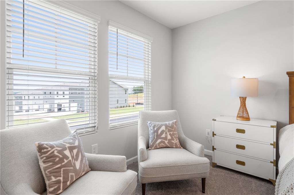 Cozy bedroom corner with cream armchairs, brass-trimmed white dresser, lamp, and window views in Davidson Homes The Durant A, Emerson, GA