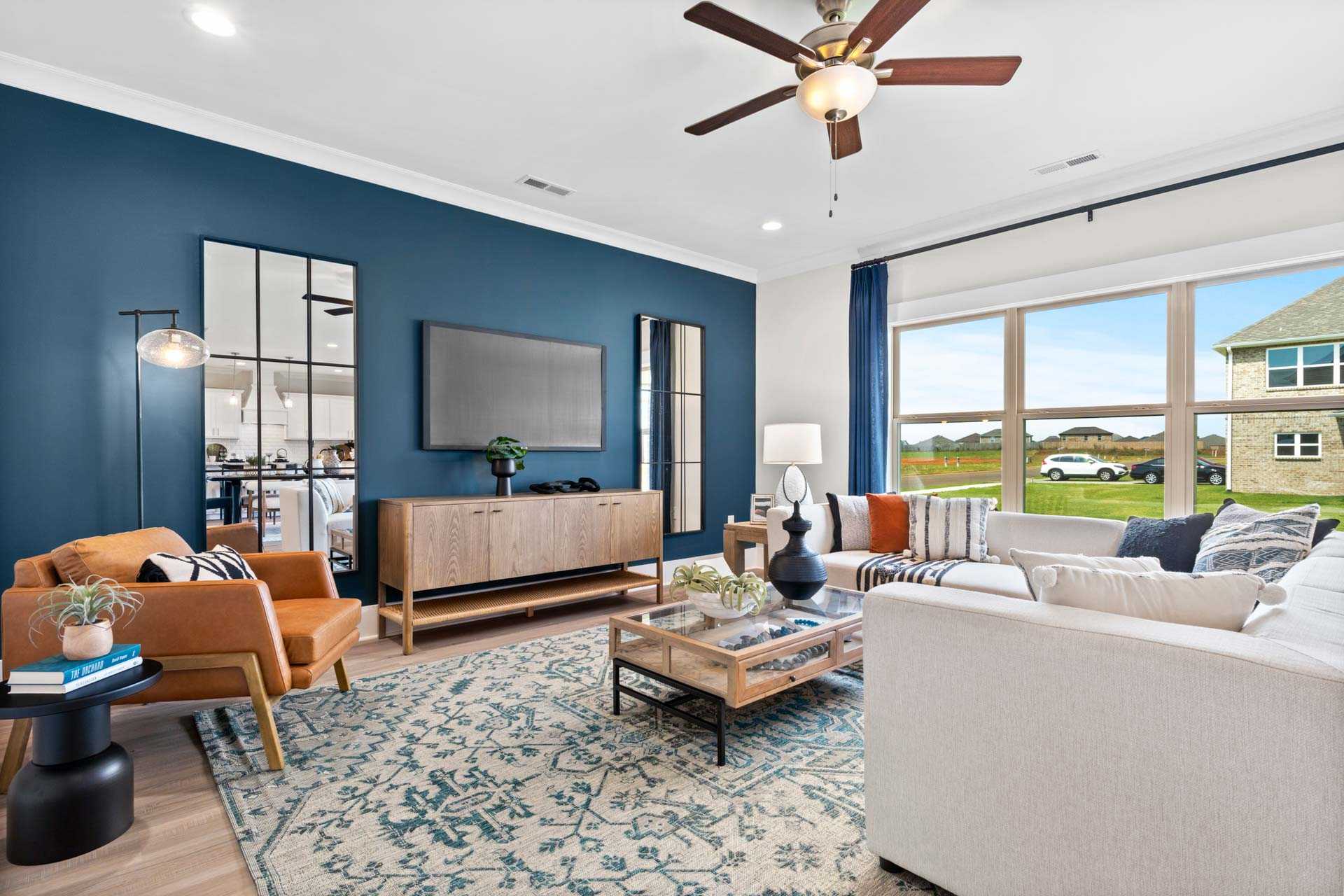 Modern living room at Walker's Hill in Meridianville Alabama with navy walls, orange armchair, white sofa, mirrors, and large windows