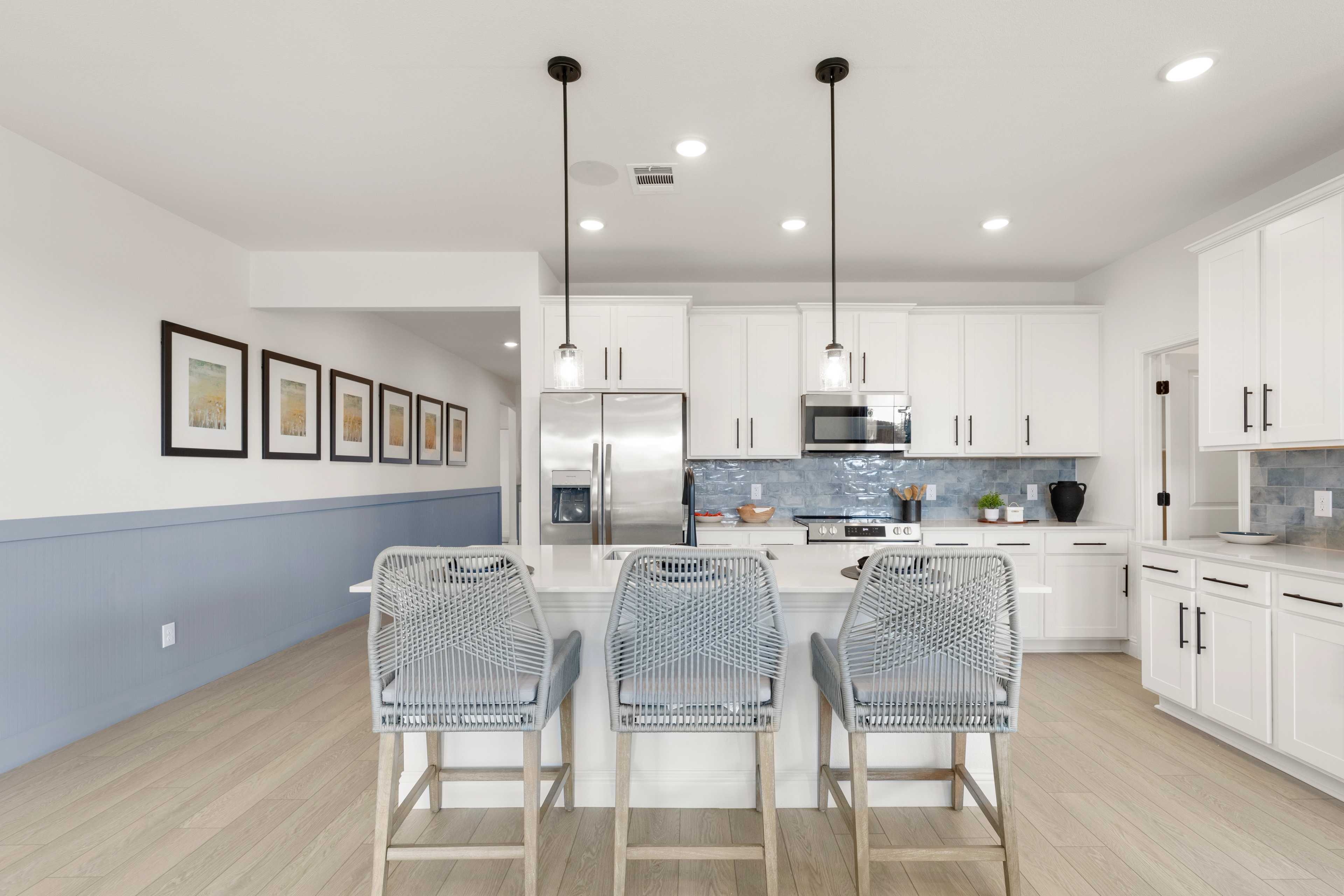 Spacious kitchen in The Laurel by Davidson Homes featuring white shaker cabinets, large island with rattan stools, stainless appliances, and blue accents