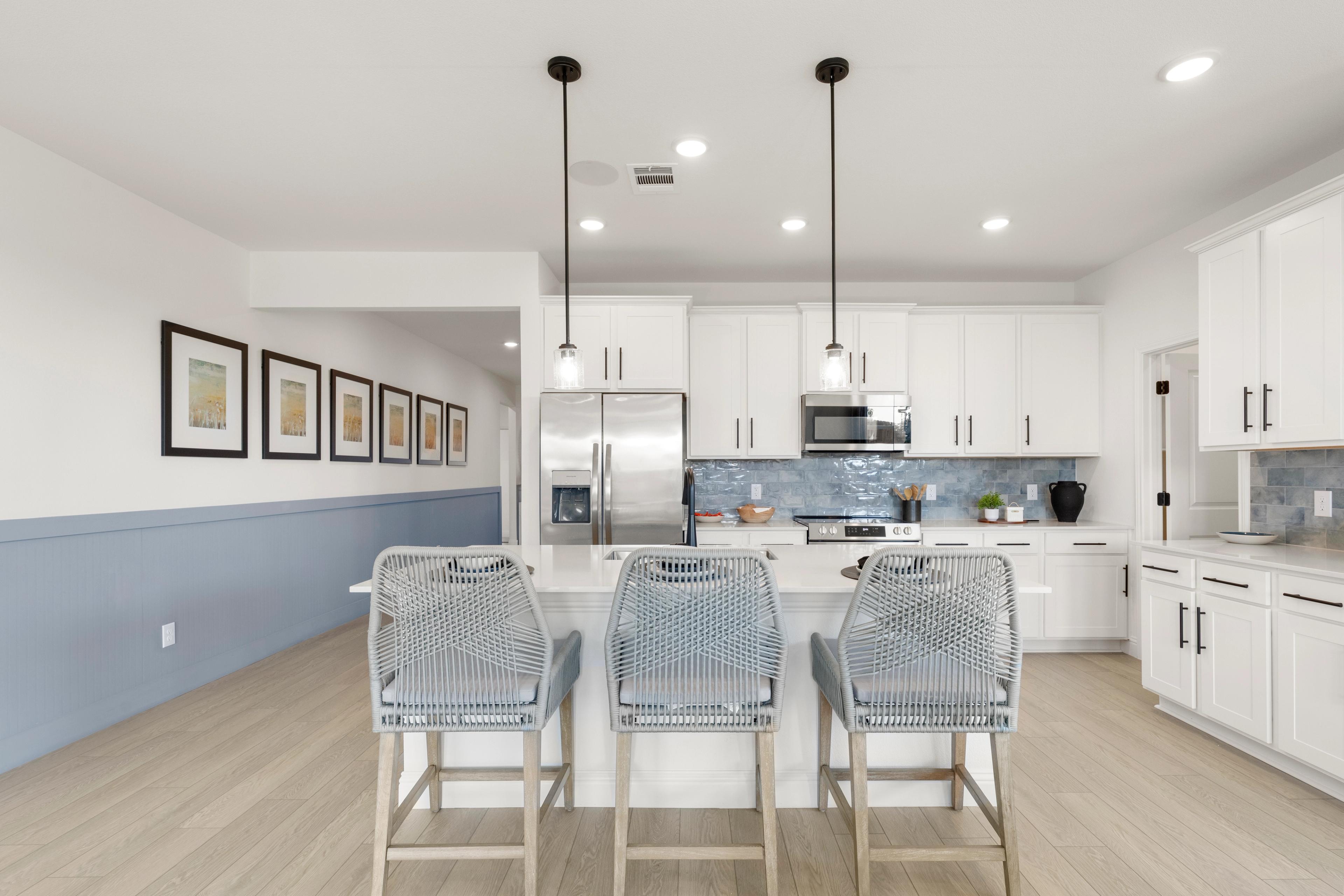 Modern kitchen in The Laurel G featuring white cabinets, large island with rattan stools, stainless appliances, blue accents