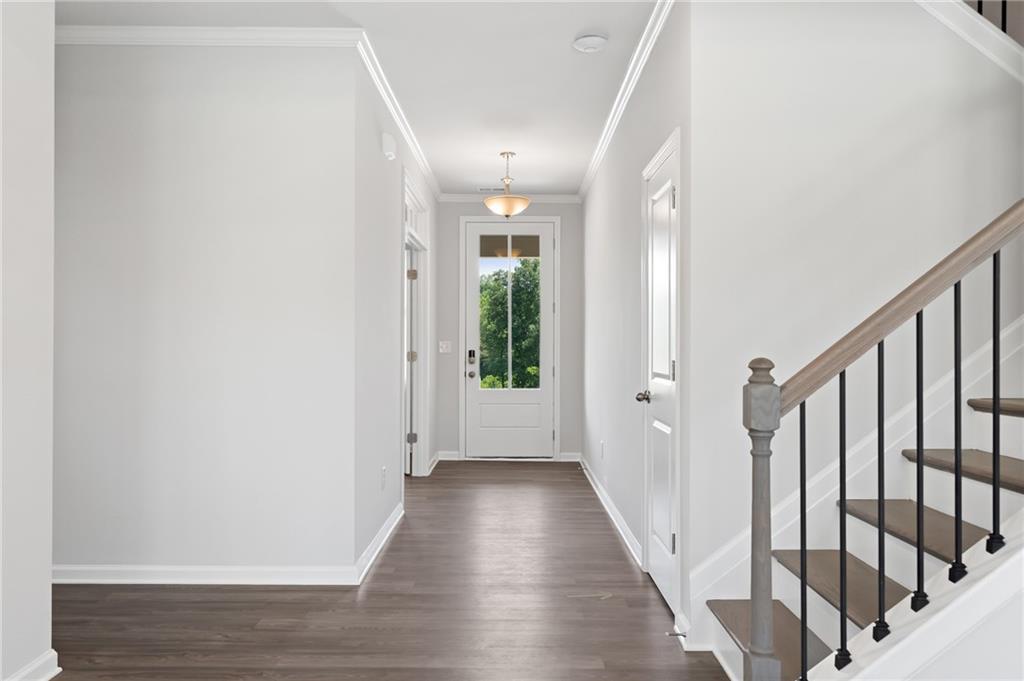 Bright foyer hallway with white walls, hardwood floors, glass-front door, and oak staircase in Davidson Homes The Hickory A, Winder, GA