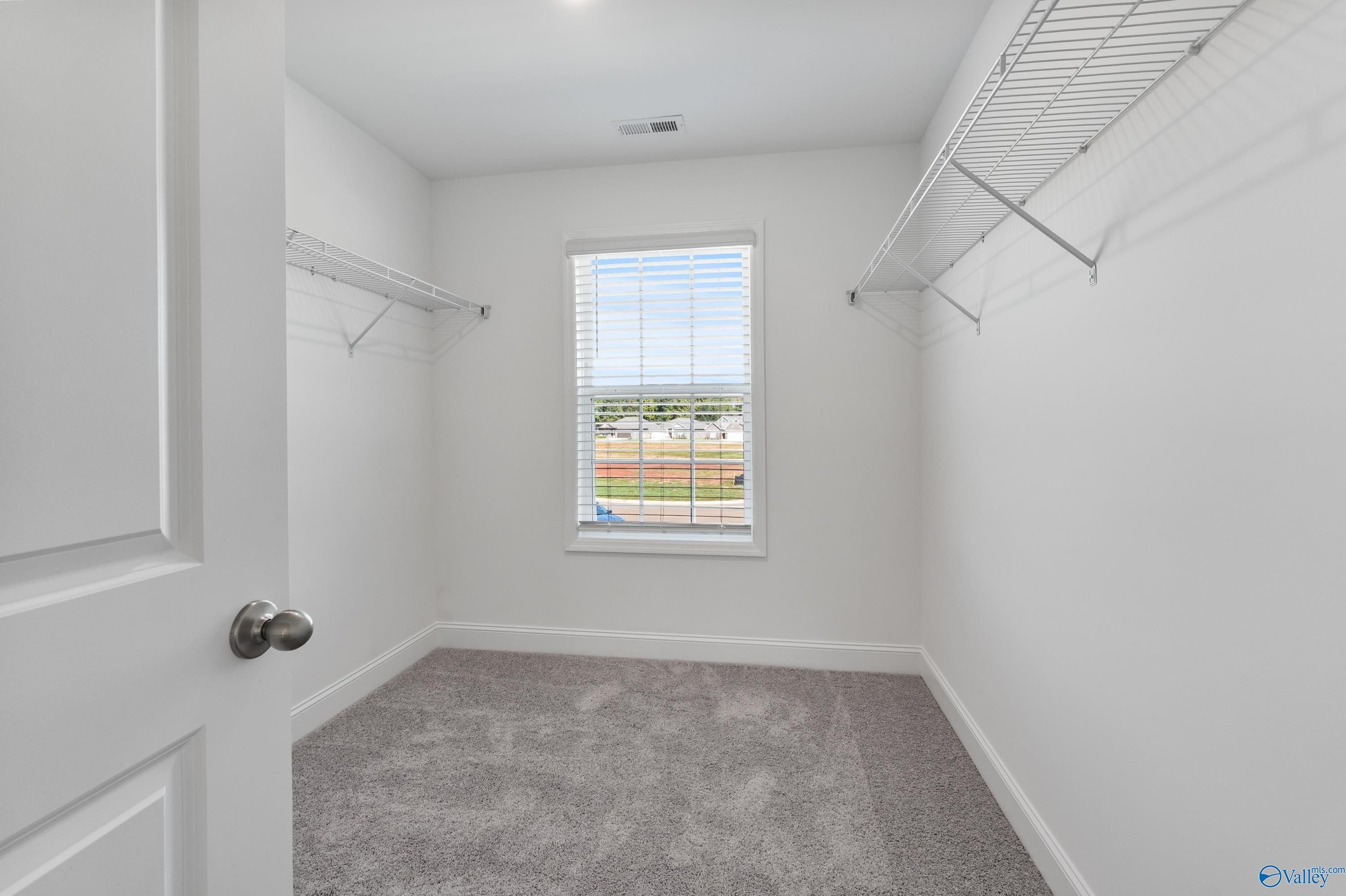 Spacious walk-in closet with wooden shelves, hanging rods, and window view in Davidson Homes The Shelby A, Athens, Alabama