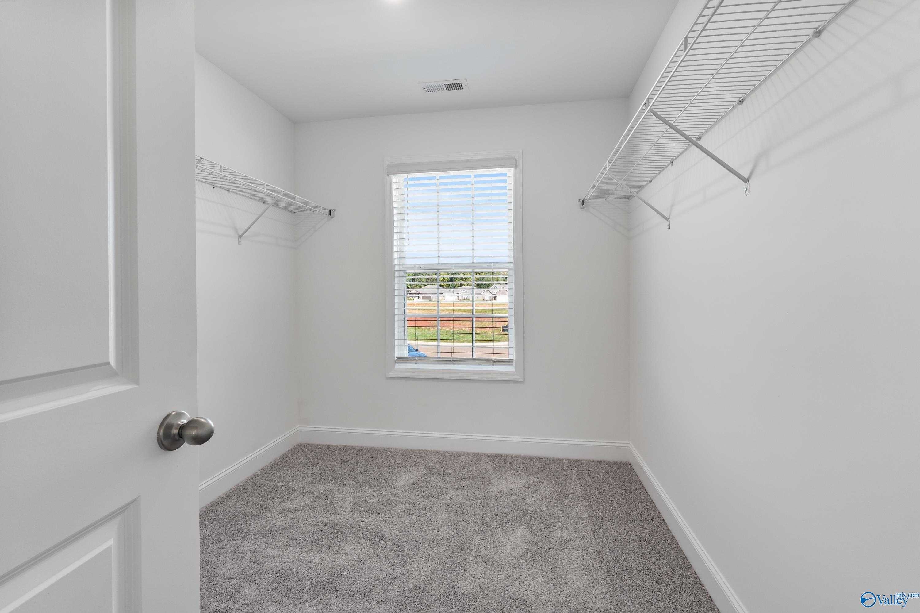 Spacious walk-in closet with built-in shelving, hanging rods, and window view in Davidson Homes The Shelby A, Athens, Alabama