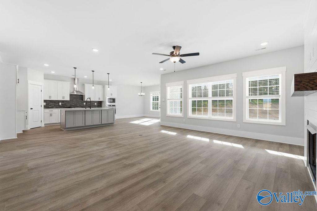 Bright open-concept living room with gas fireplace, hardwood floors, large windows, and adjacent kitchen in Davidson Homes The Rockford, Hartselle, Alabama