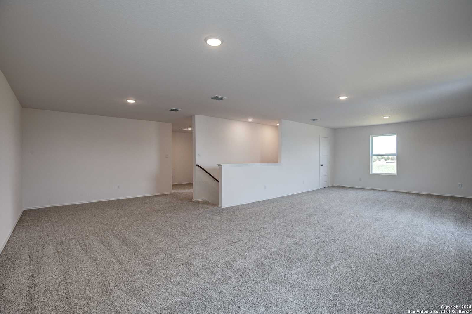 Spacious upstairs loft with gray carpet flooring, recessed lighting, and open staircase in Davidson Homes The Douglas D, Seguin, Texas