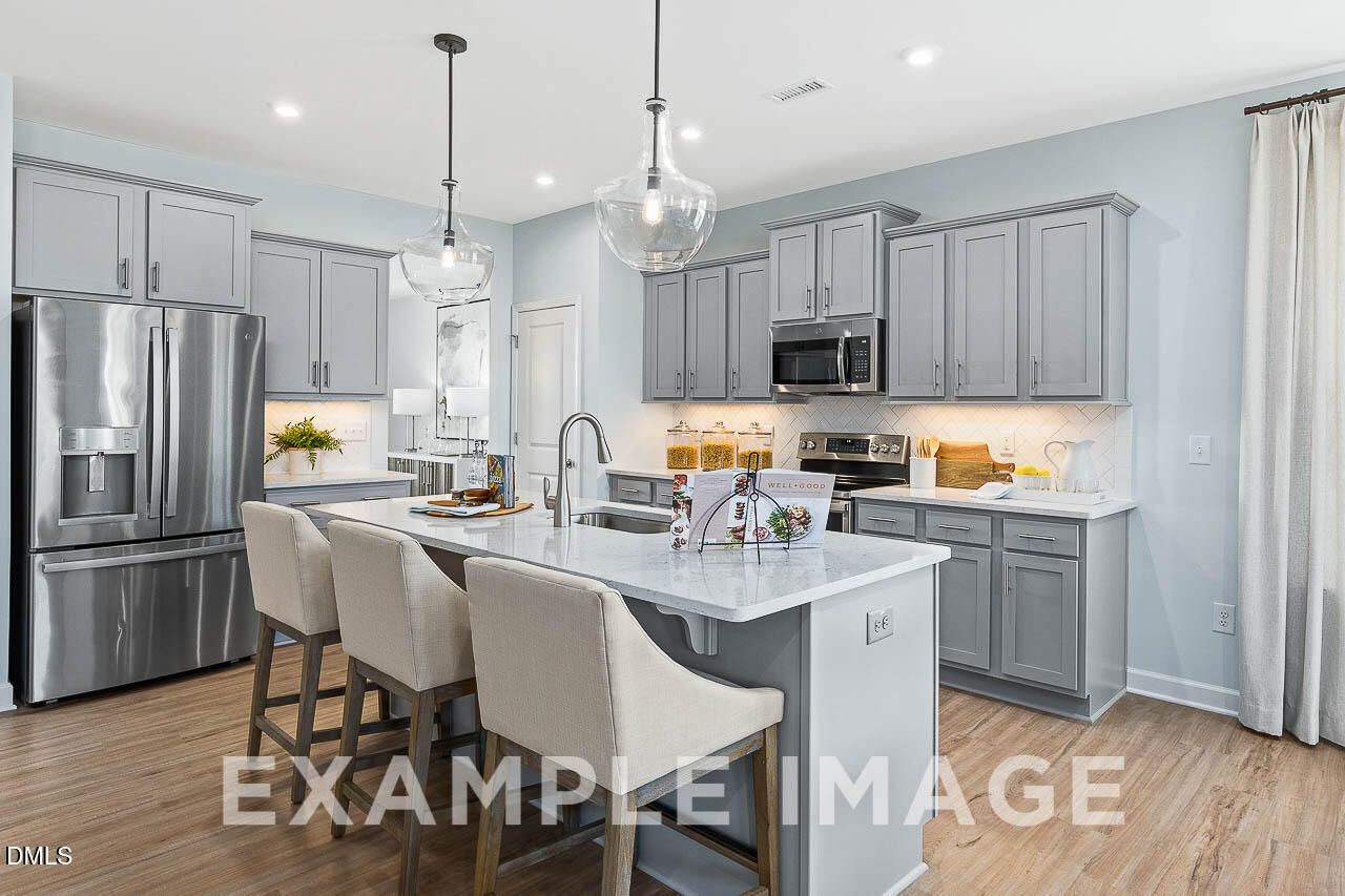 Modern kitchen with gray shaker cabinets, marble island, pendant lights, and stainless appliances in Davidson Homes The Ash C, Lillington NC